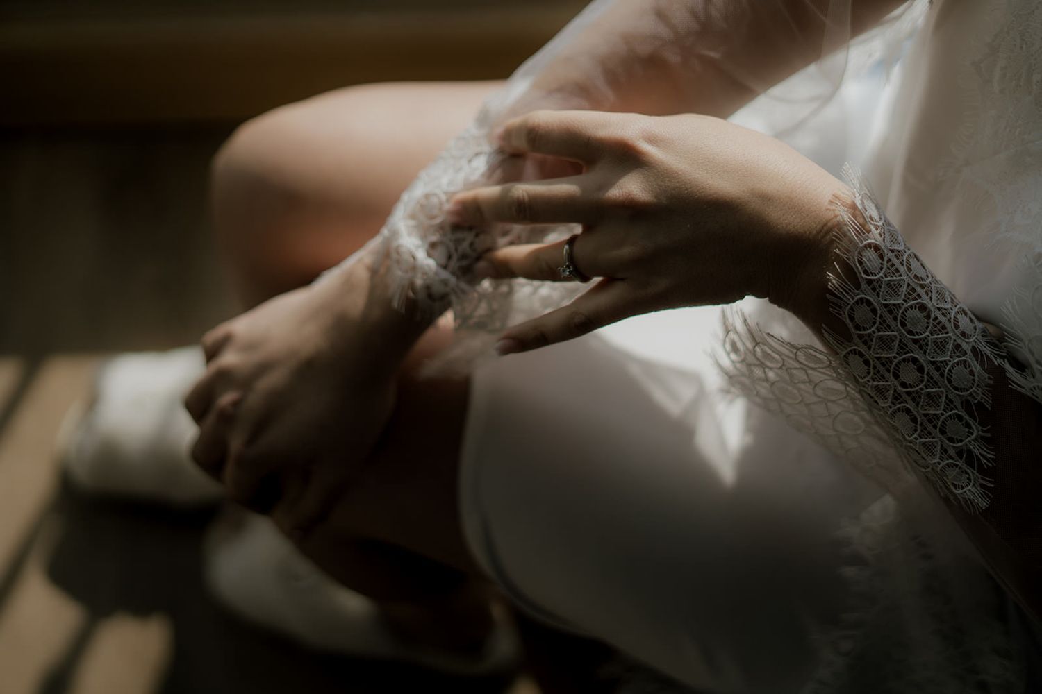 Close-up of bride wearing lace robe and diamond engagement ring in warm sunlight.