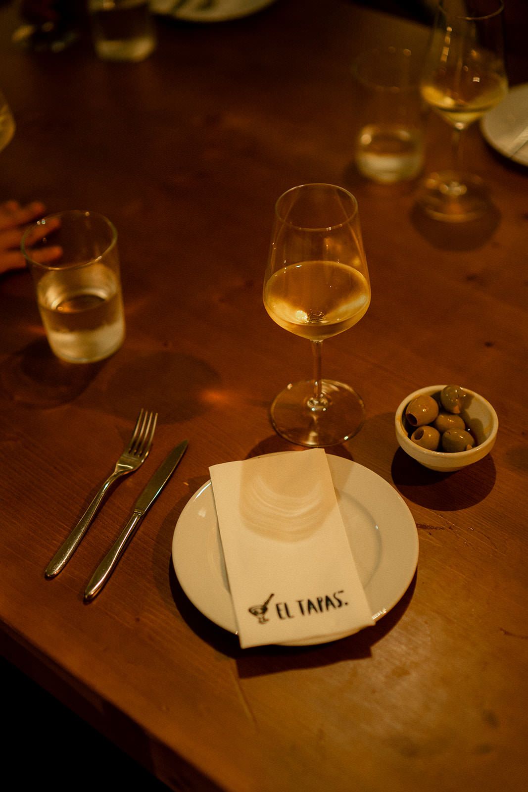 Dimly lit restaurant table setting with wine glasses and place settings in warm ambient lighting.