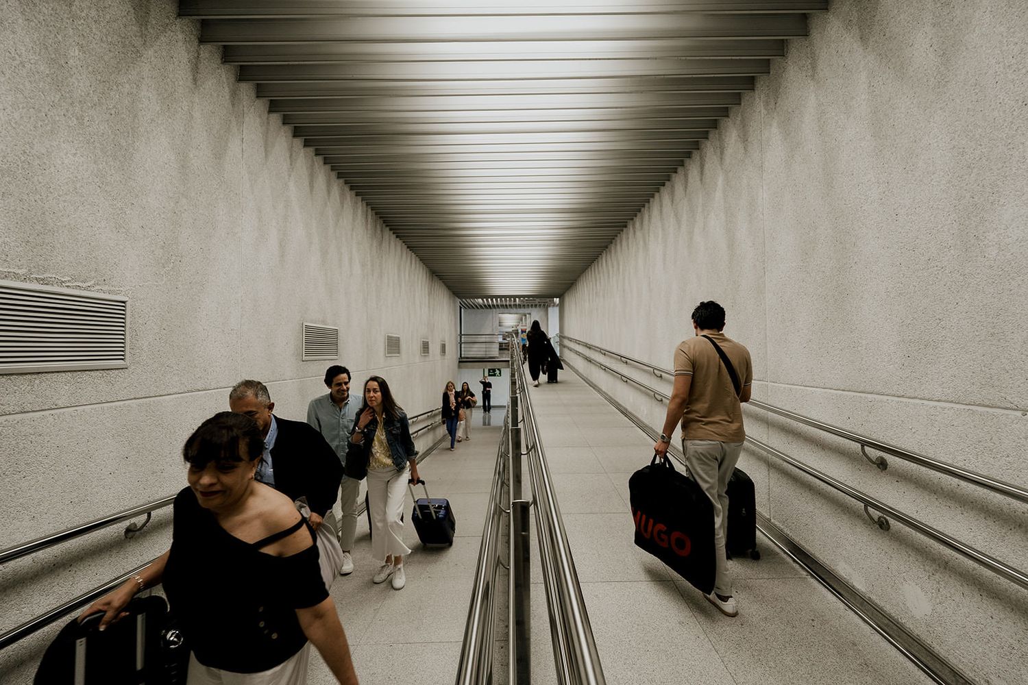 Long concrete corridor with sloped walls and artificial lighting creating a modern minimalist architectural perspective.