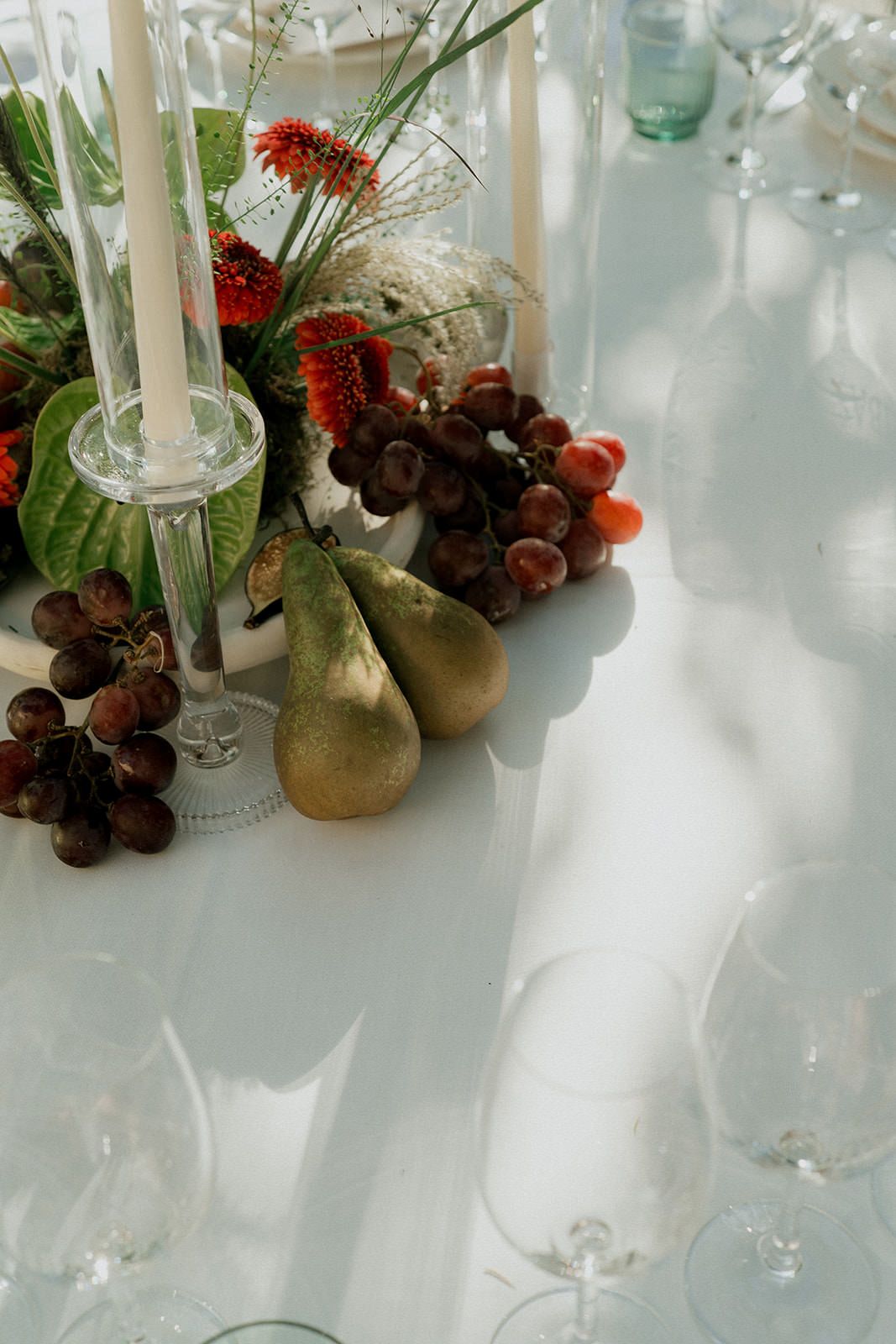Elegant table setting with white candles, red flowers, and rustic decorative elements on a light tablecloth.
