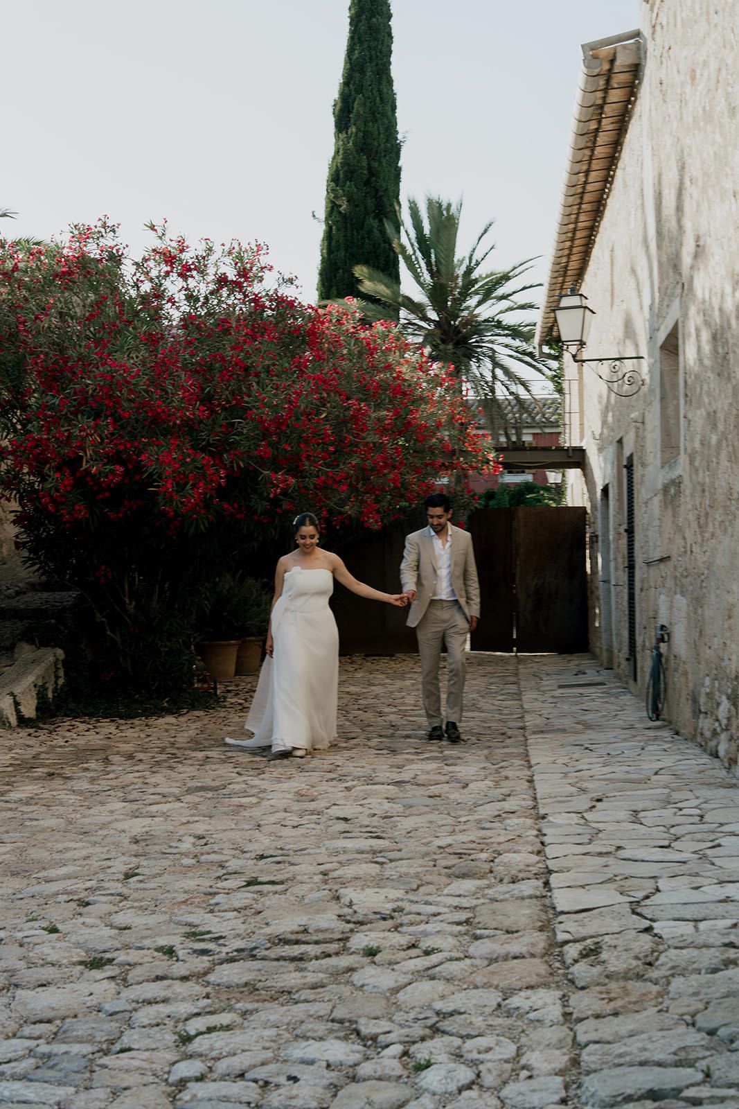 A cobblestone courtyard with red flowering bushes and Mediterranean architecture creates a romantic setting.