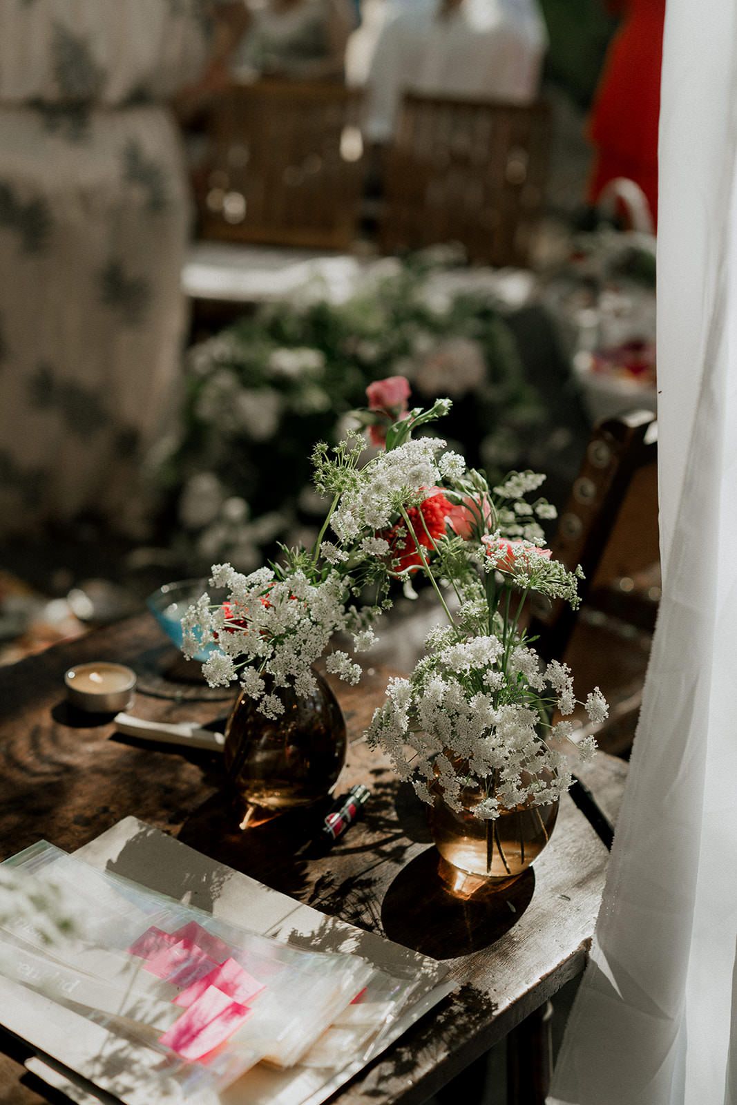 Delicate white floral arrangements in dark glass vases sit atop a rustic table with scattered papers and decor.