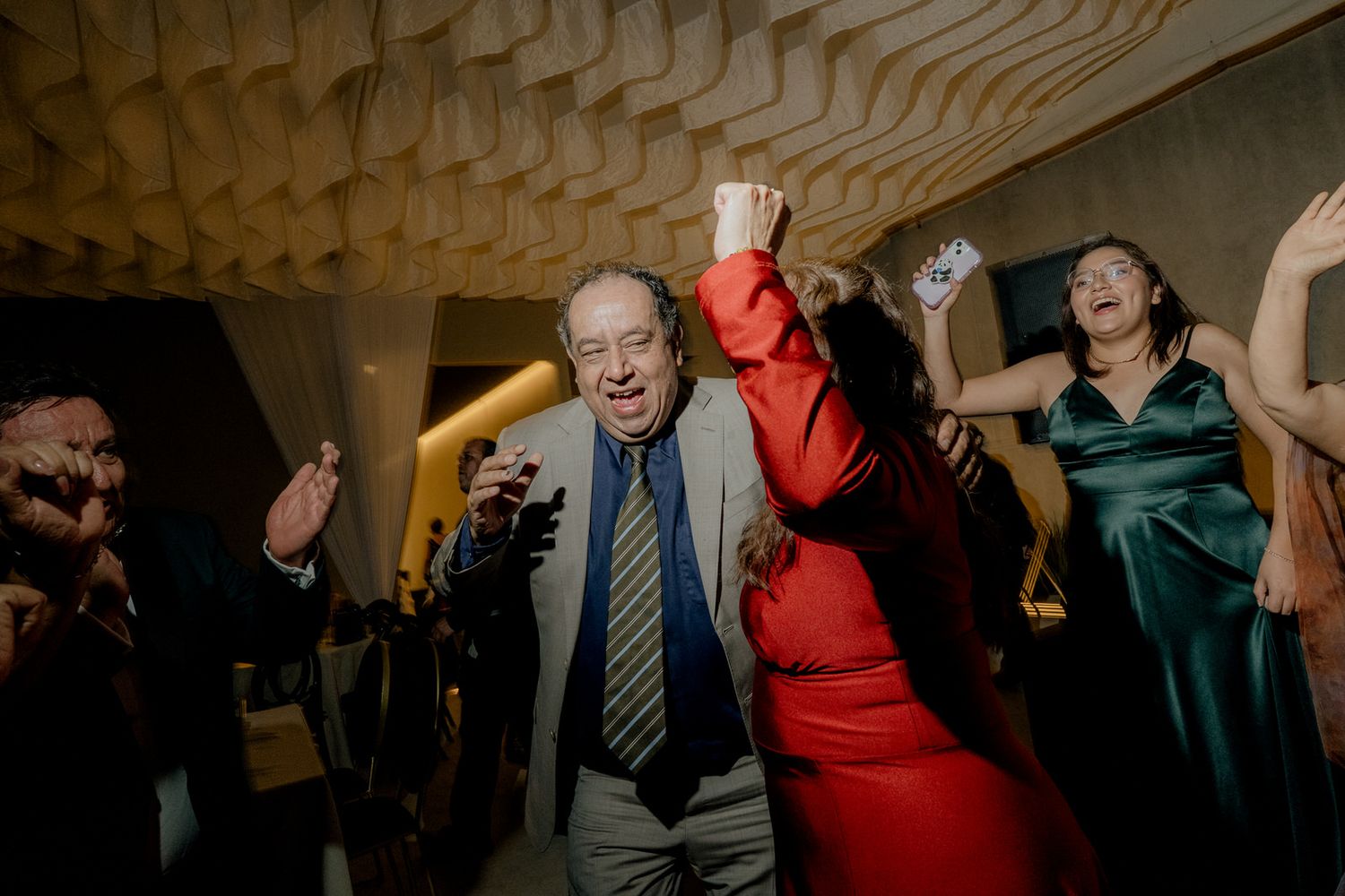 Energetic wedding guest in red dress dances enthusiastically during lively wedding reception party.