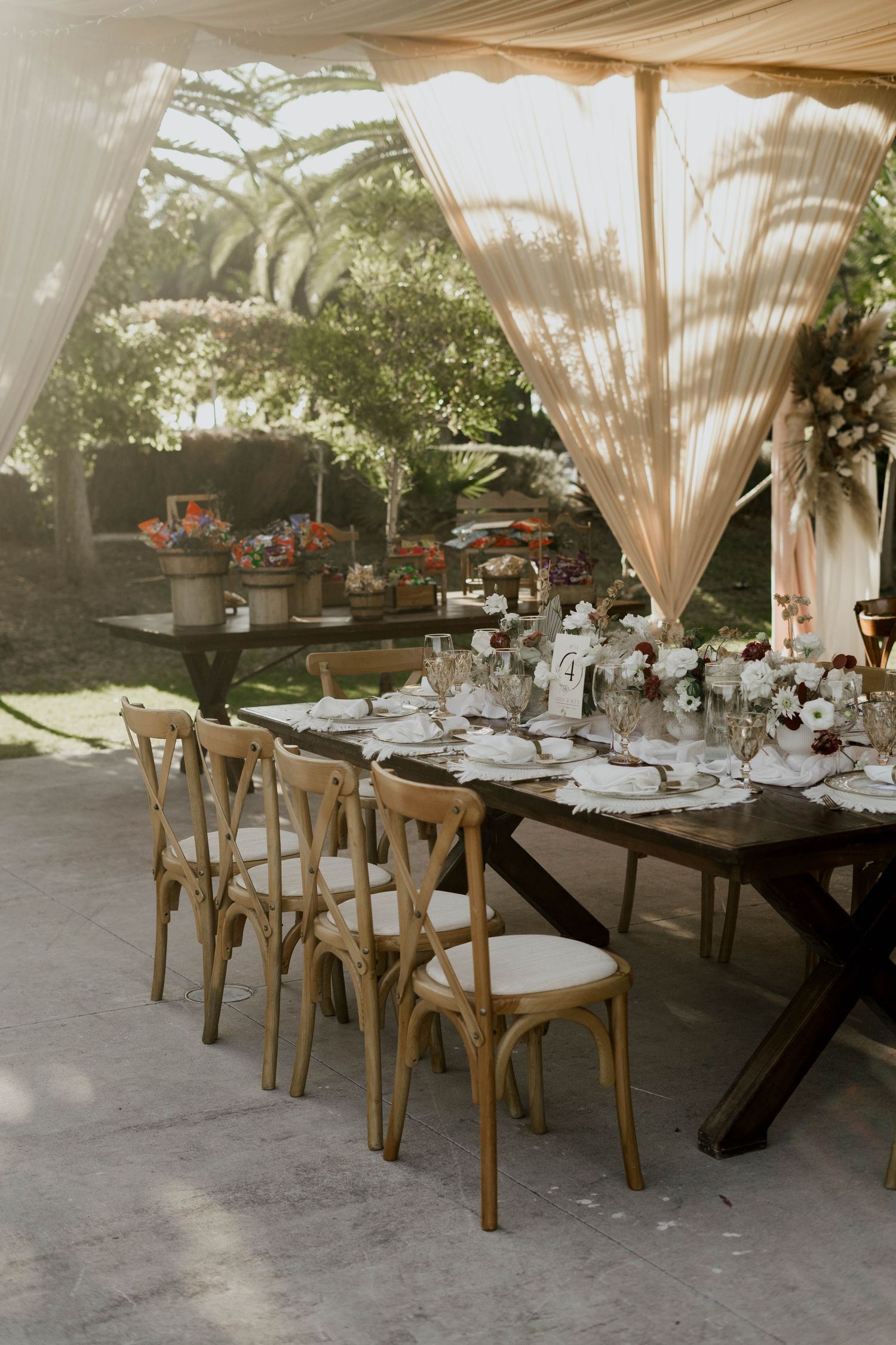 Elegant outdoor wedding reception setup with wooden chairs and draped fabric canopy.