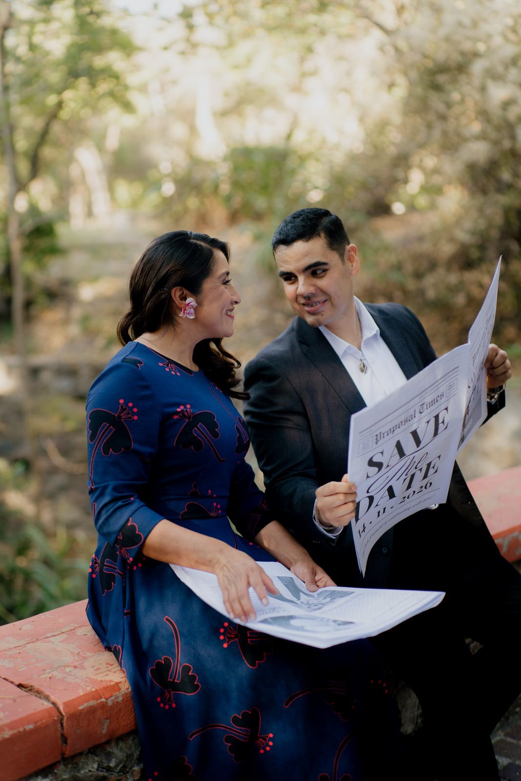 A couple looks at each other while holding save-the-date cards outdoors.