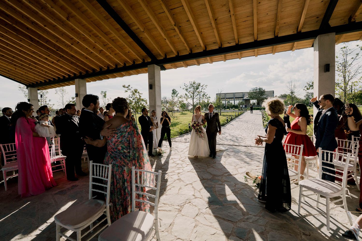 Panoramic view of wedding ceremony under covered outdoor pavilion with wooden ceiling beams.