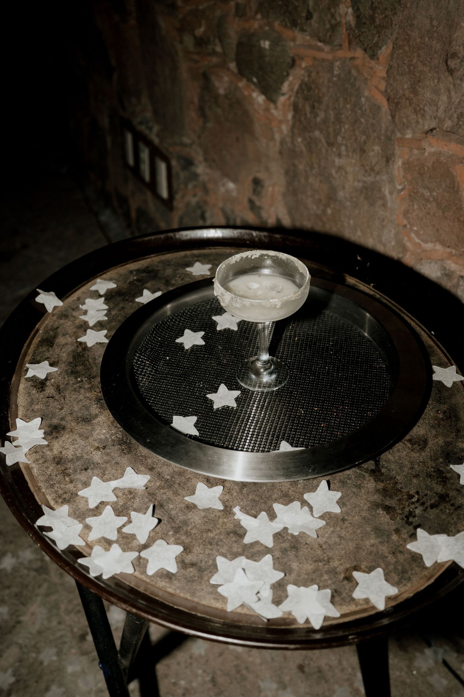A cocktail glass sits on a dark table decorated with scattered star-shaped confetti.