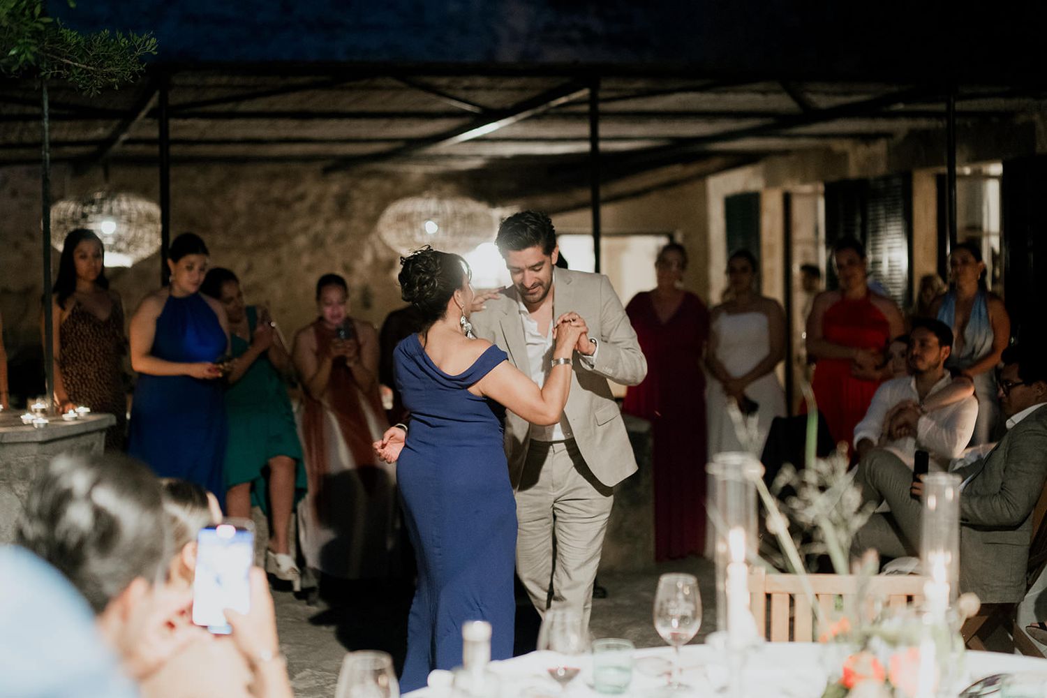 Wedding guests dancing and celebrating at an indoor reception venue with atmospheric lighting.