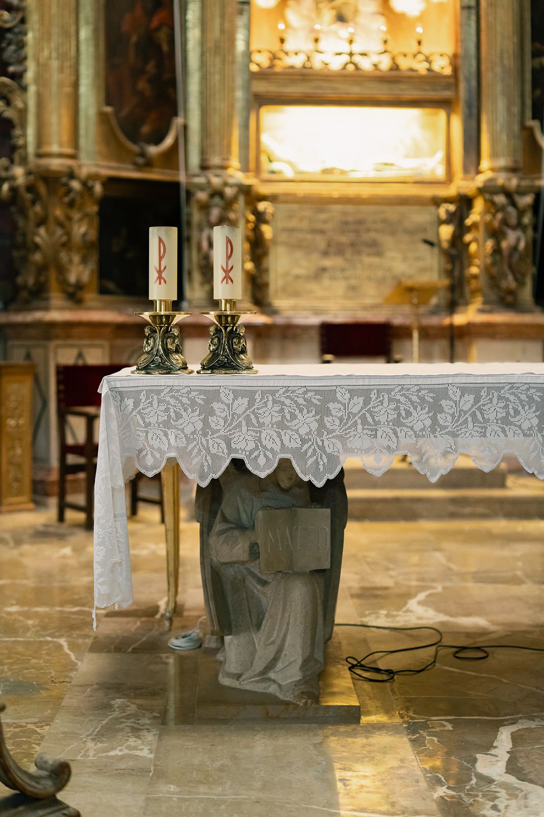 Ornate church altar with lace tablecloth and golden details illuminated by warm lighting.