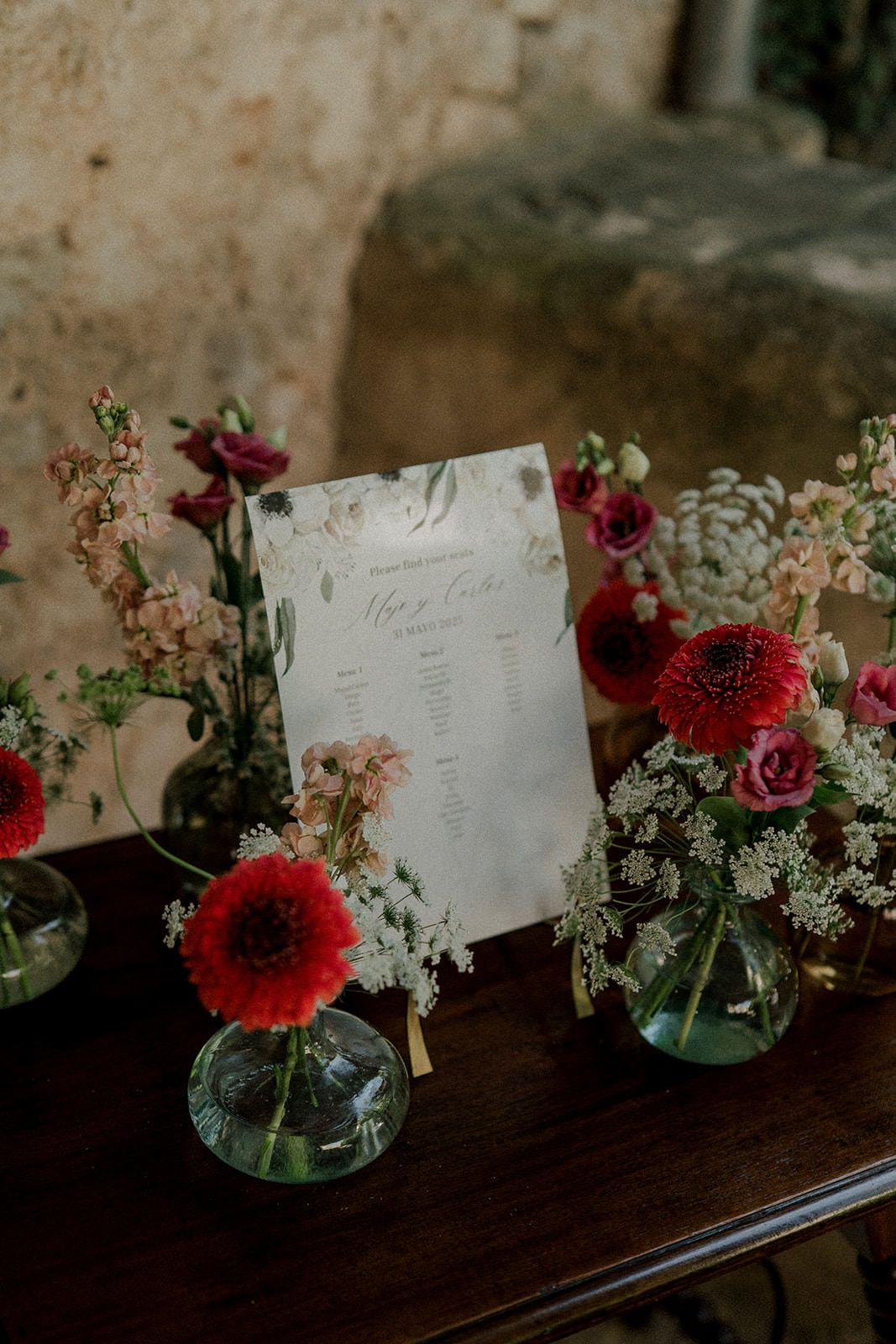 Red and pink floral arrangements with handwritten place cards displayed on a dark wooden surface for an elegant event.
