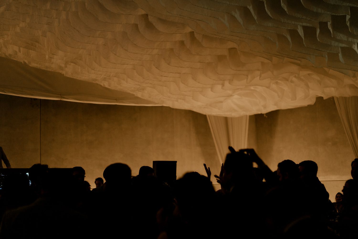 Wedding guests silhouetted against dramatic sculptural ceiling with warm golden ambient lighting.