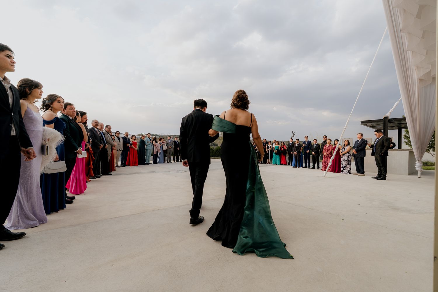 Wedding guests line up outdoors as couple in formal attire walks through crowd at elegant reception.