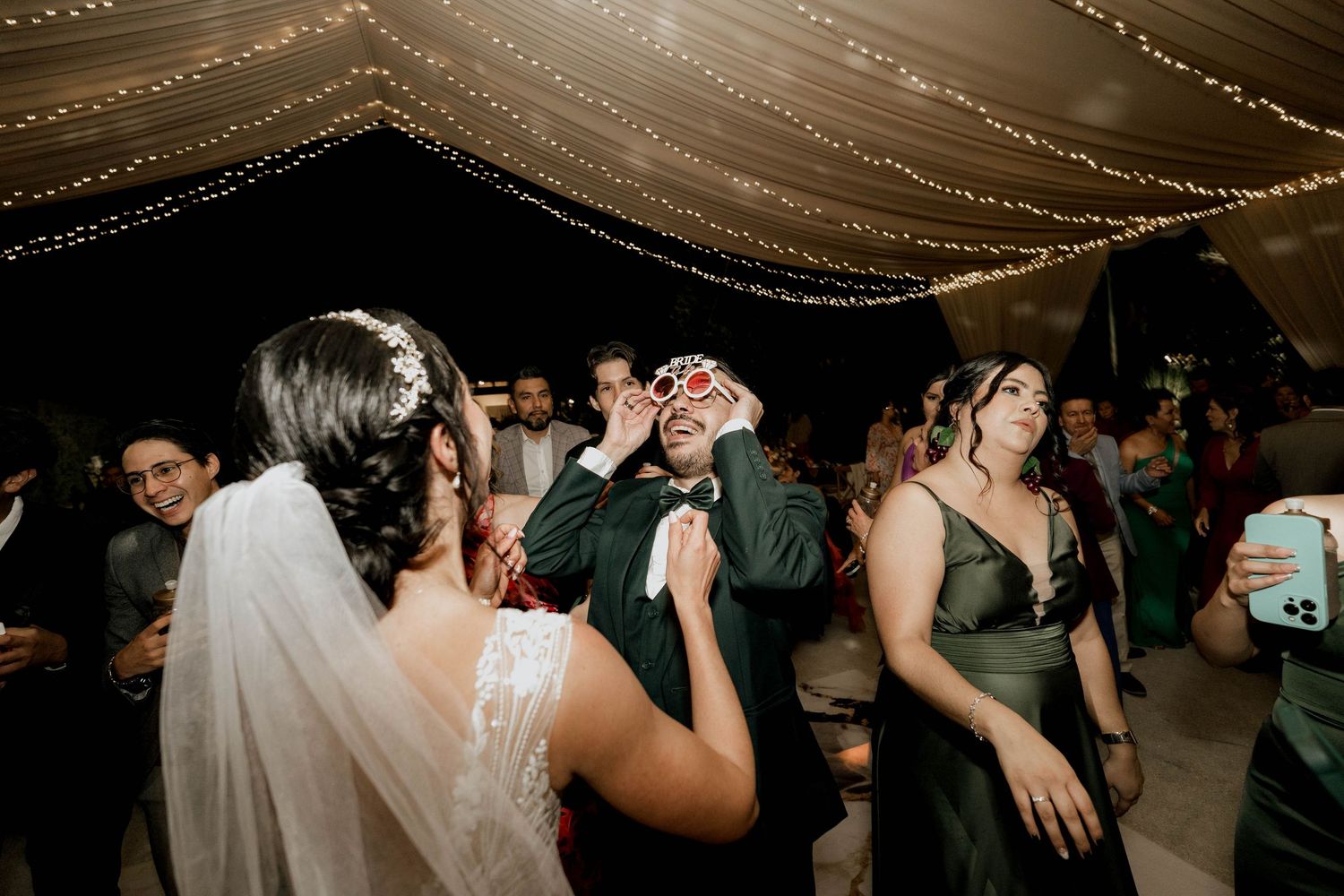 Wedding guests dancing and celebrating under draped fabric ceiling with string lights.