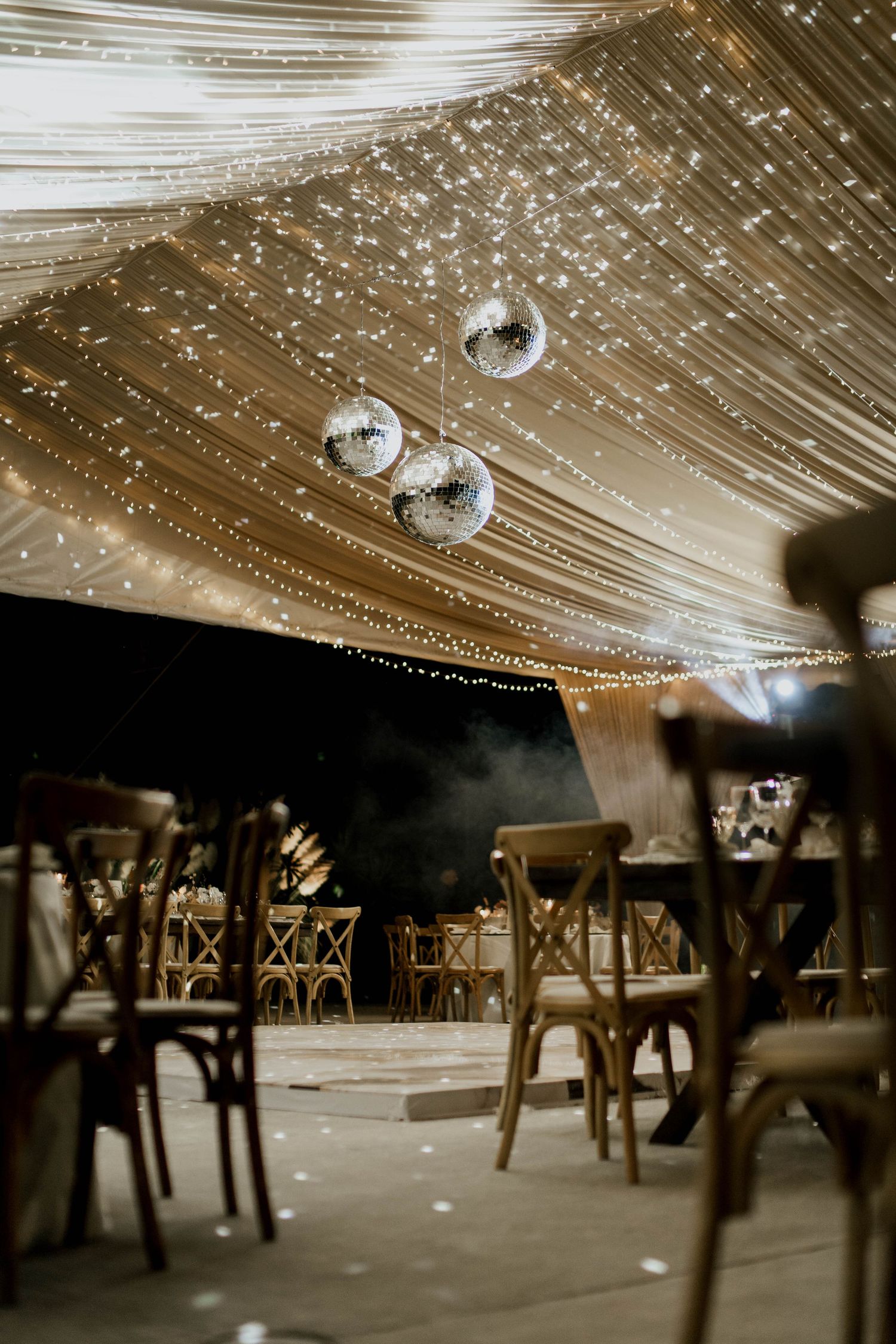Wedding venue decorated with hanging disco balls, string lights and white fabric creating a celestial effect.