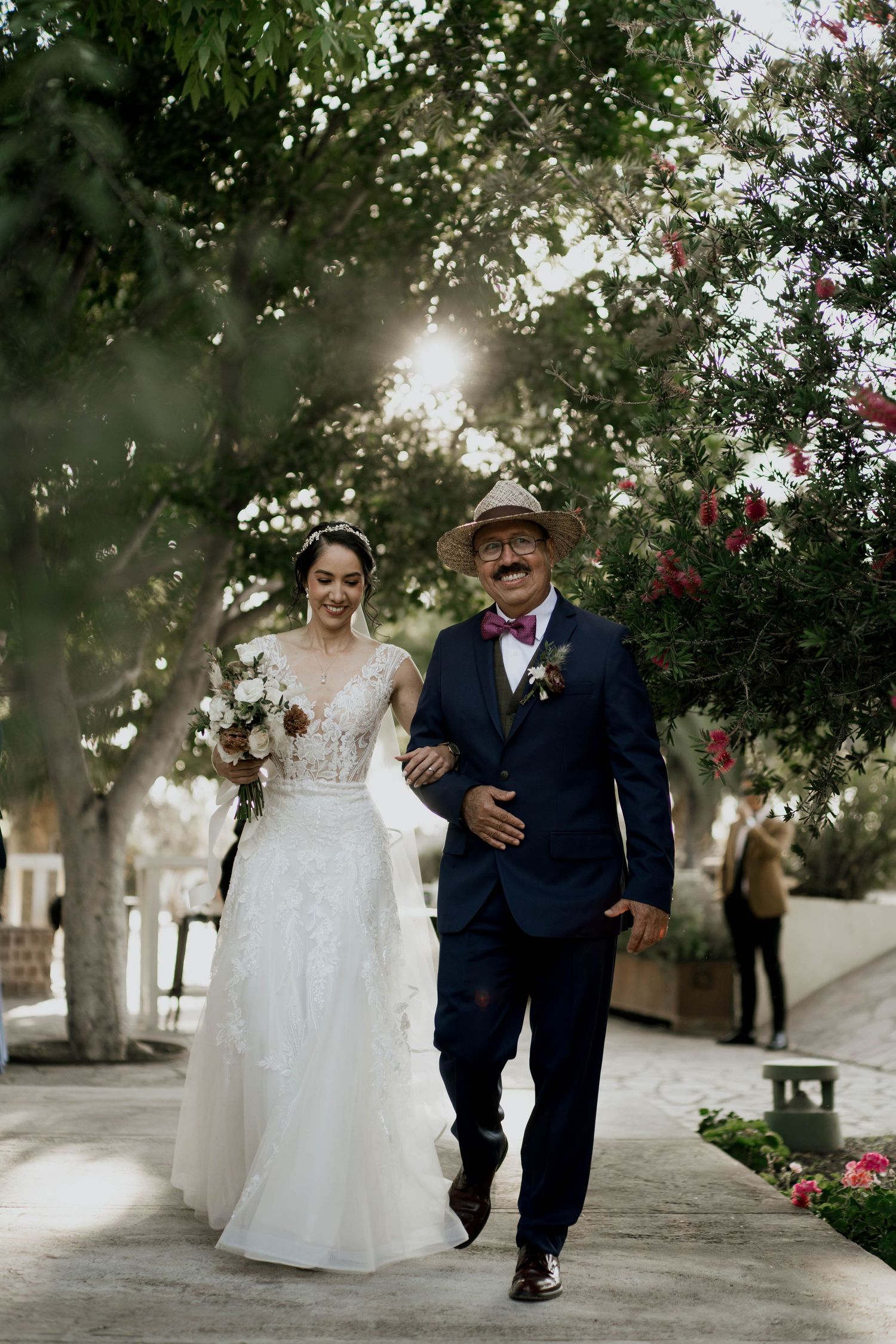Couple walks along stone pathway surrounded by blooming trees and flowers.
