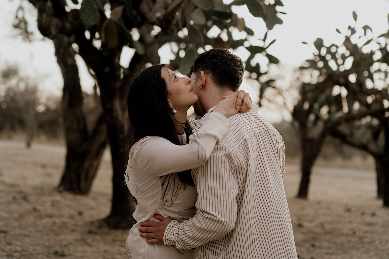 A romantic couple embraces while dancing in an outdoor setting with trees.