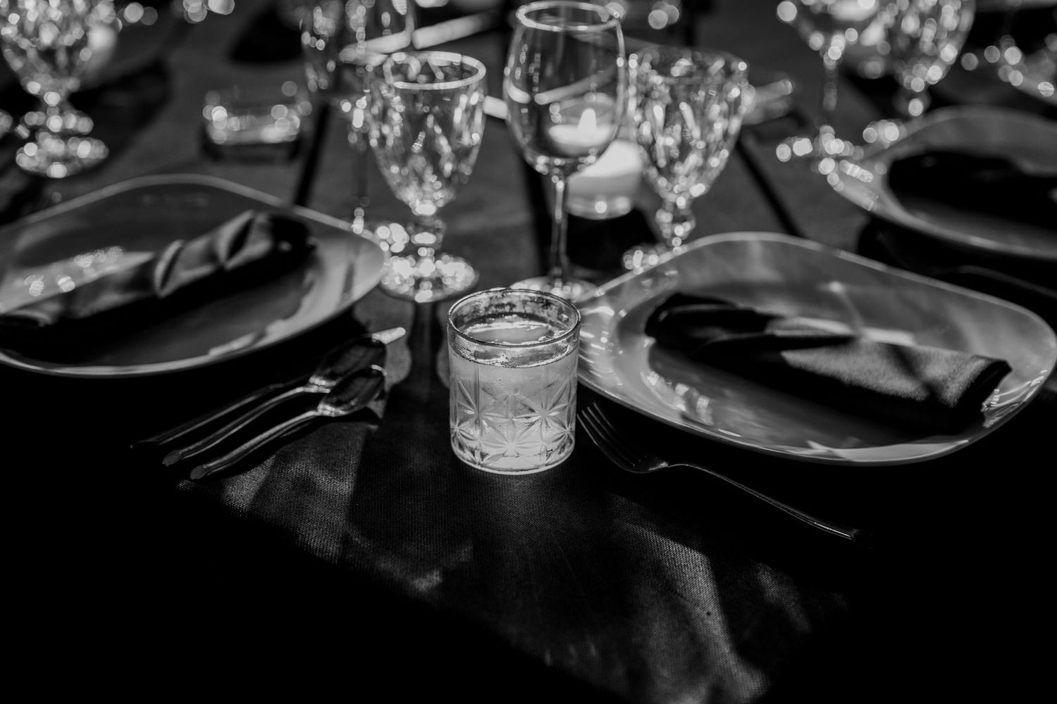 Black and white detail of elegant place settings with wine glasses and cutlery.