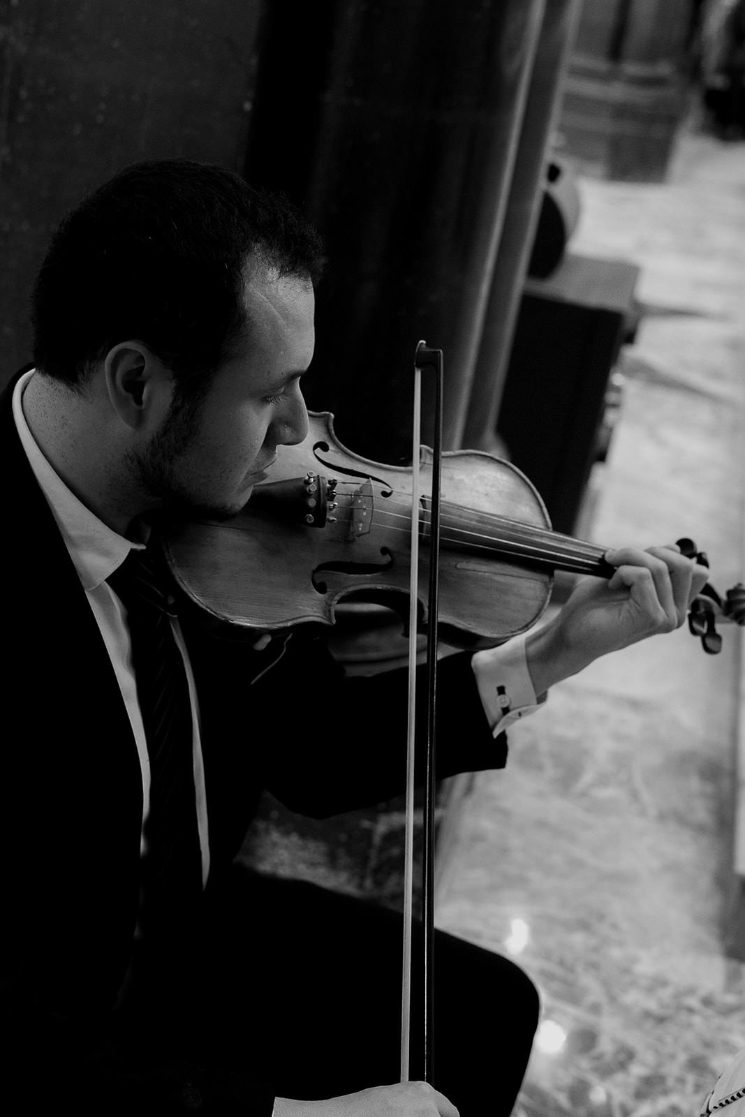 Black and white portrait of a violinist in a suit performing during an elegant wedding ceremony.