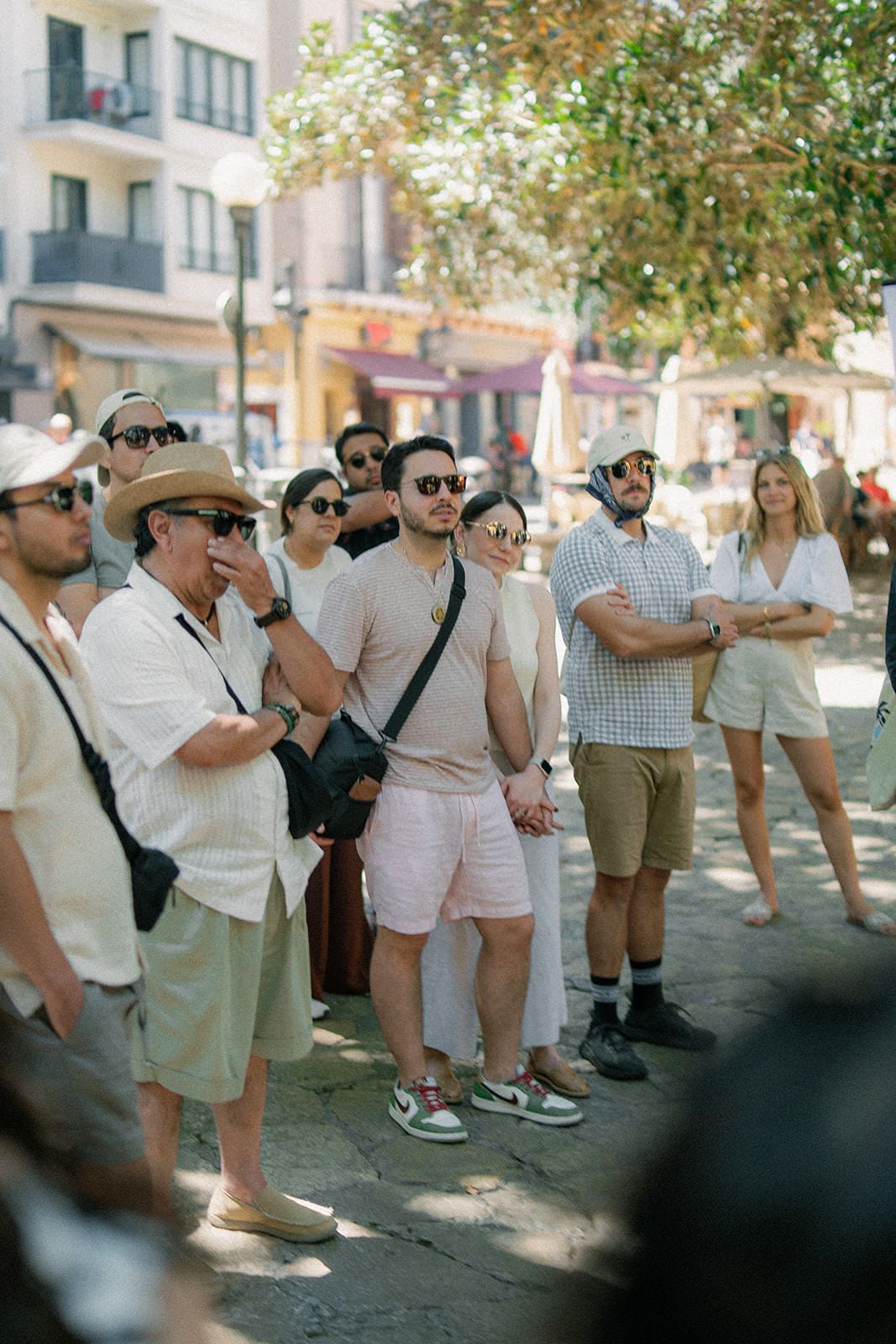 A group of tourists in casual summer attire gather on a city street during a walking tour.