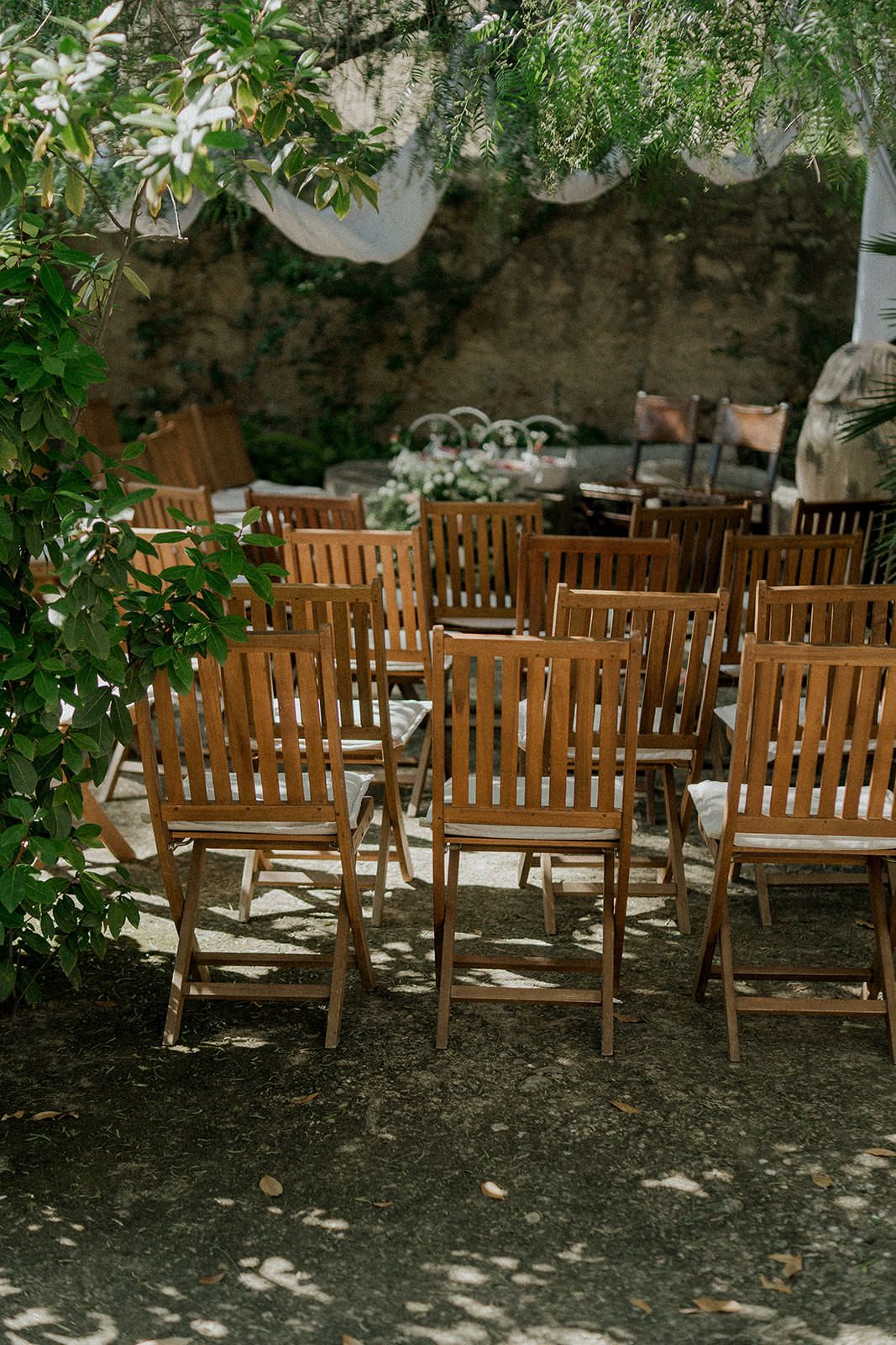 Row of wooden garden chairs arranged for outdoor wedding ceremony under tree canopy.