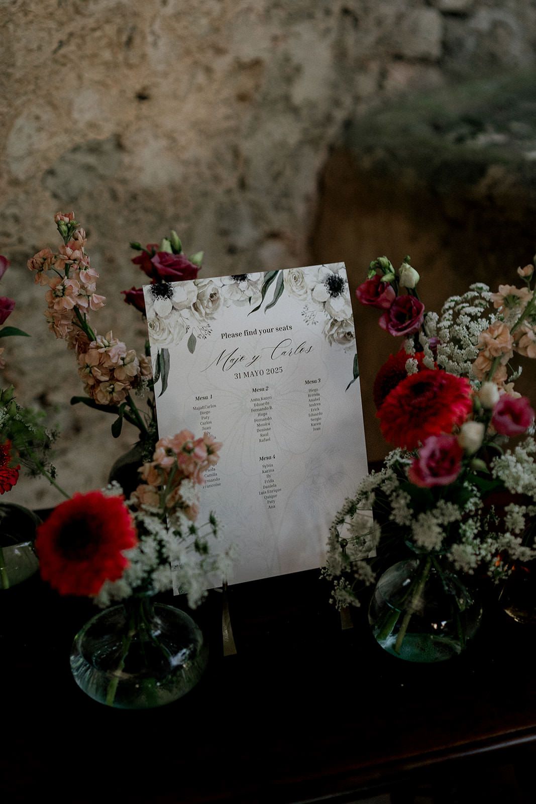 Elegant floral arrangements with red roses and white flowers alongside wedding seating cards.