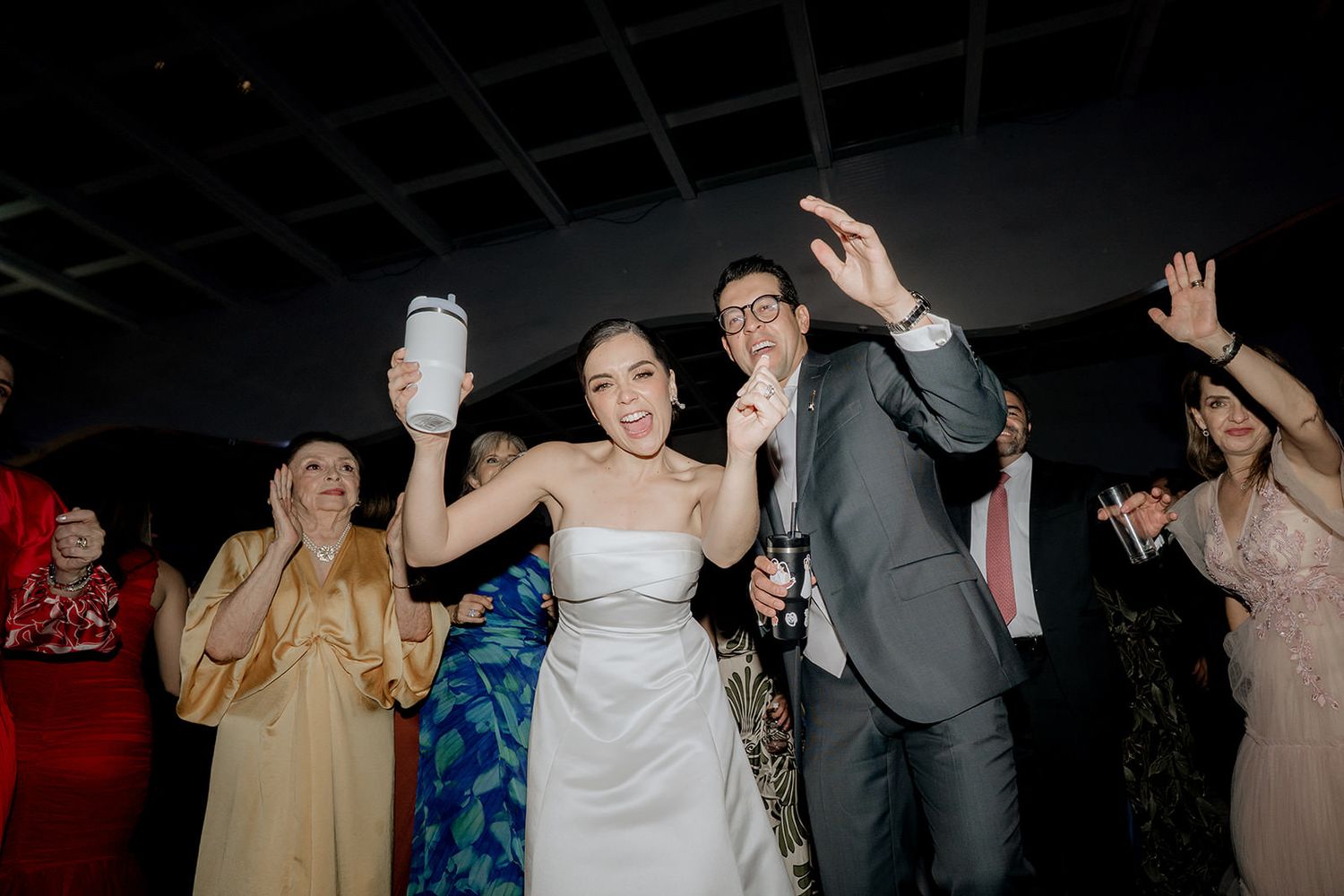 Bride and groom celebrate joyfully with guests during lively wedding reception dance.