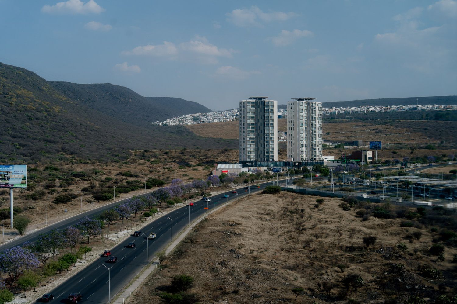 Aerial view of urban road with tall buildings and mountains in background.