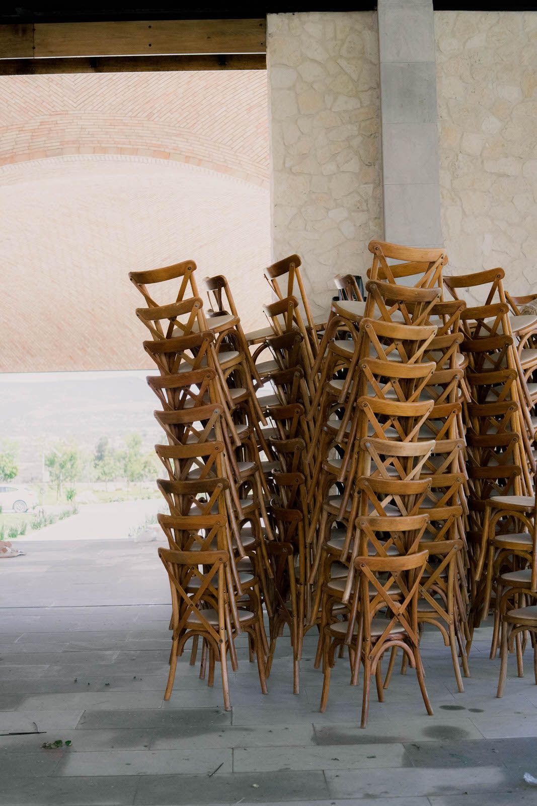 Wooden cross-back chairs stacked and arranged in rows for an event setup.