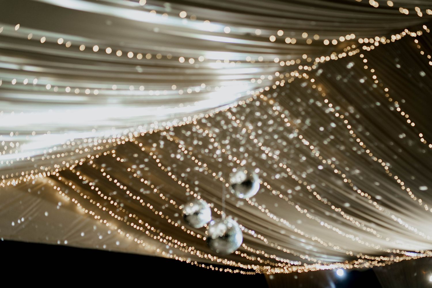 Dramatic ceiling installation of string lights and fabric creating a starry effect for an event.