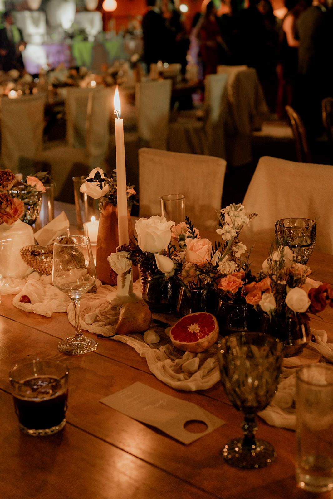 Elegant wedding reception tablescape with candles, roses, and grapefruit centerpiece decor.