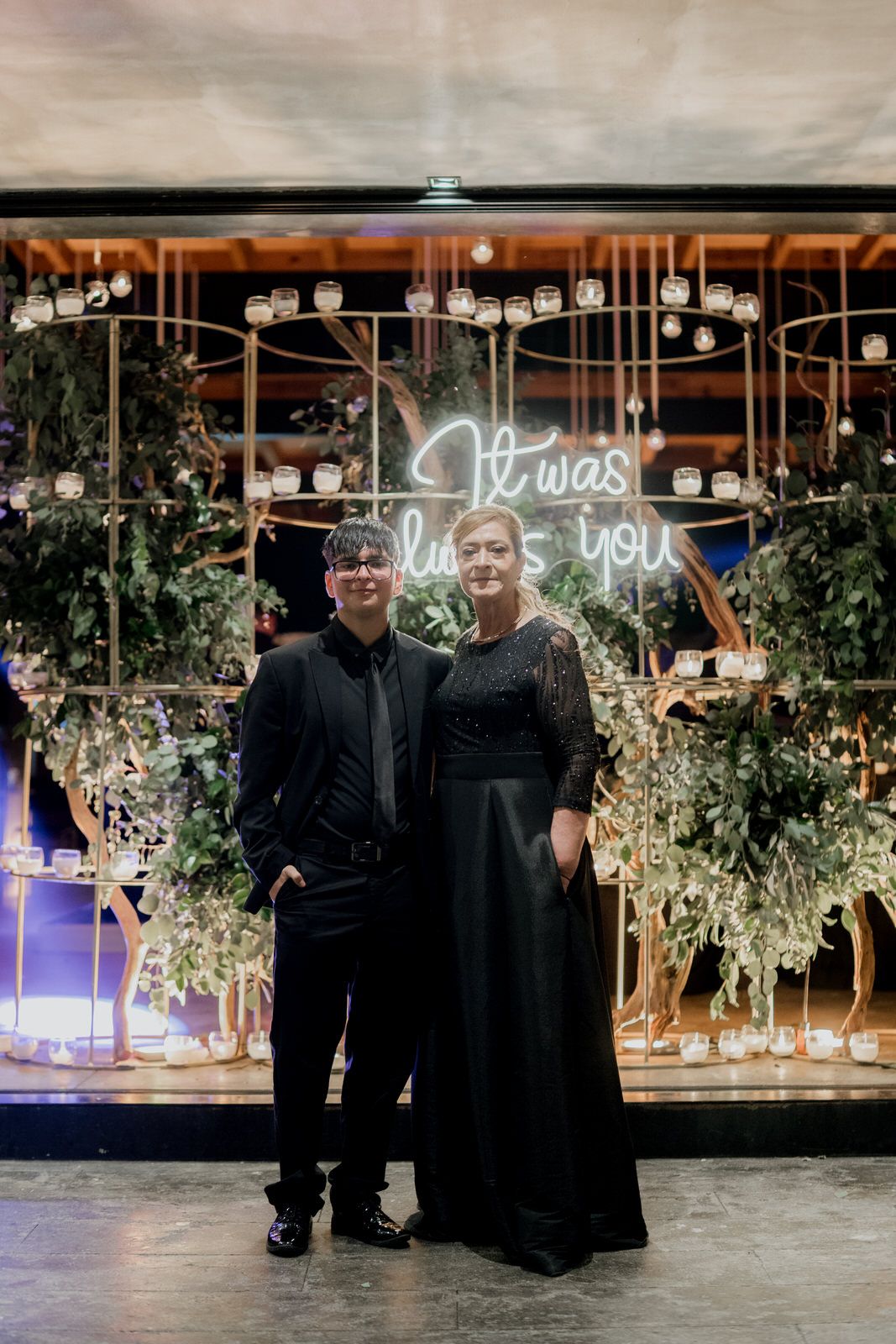 Wedding venue decorated with hanging greenery and illuminated neon signs.