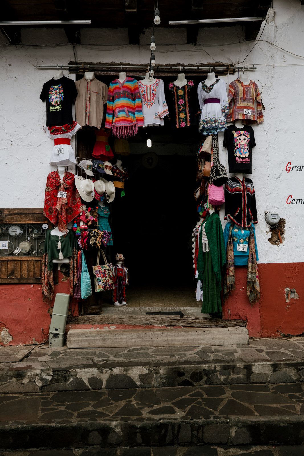 Colorful clothing and souvenirs displayed at market stalls along a stone-walled street.