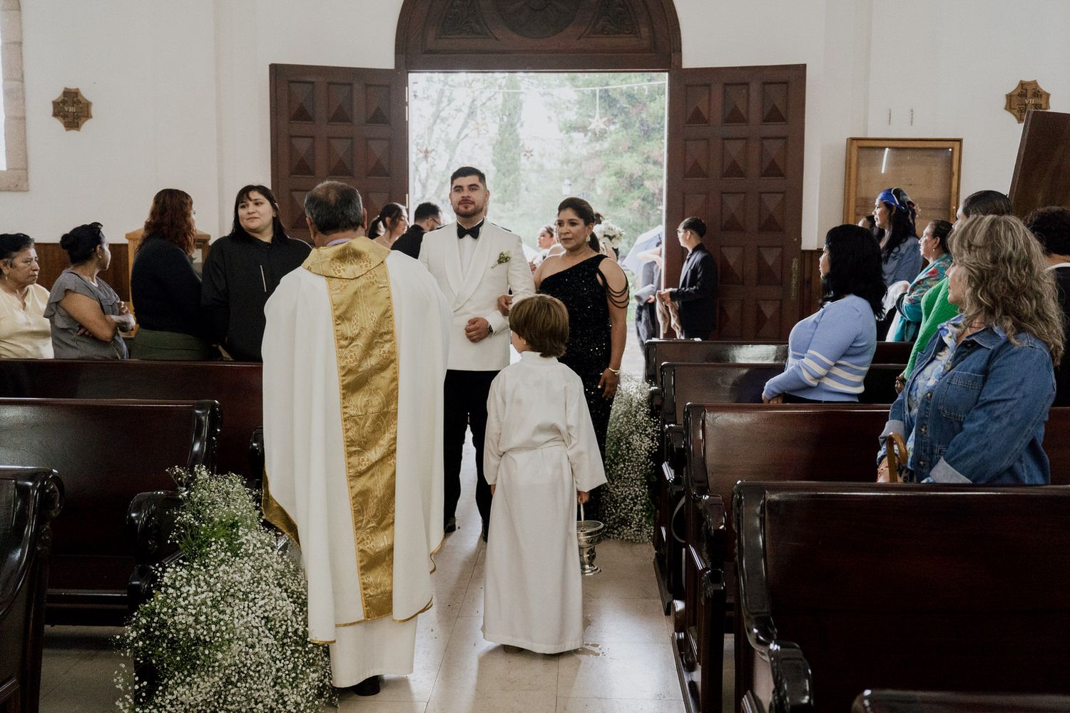 Interior of a church decorated with white flowers and wooden pews for a wedding ceremony.