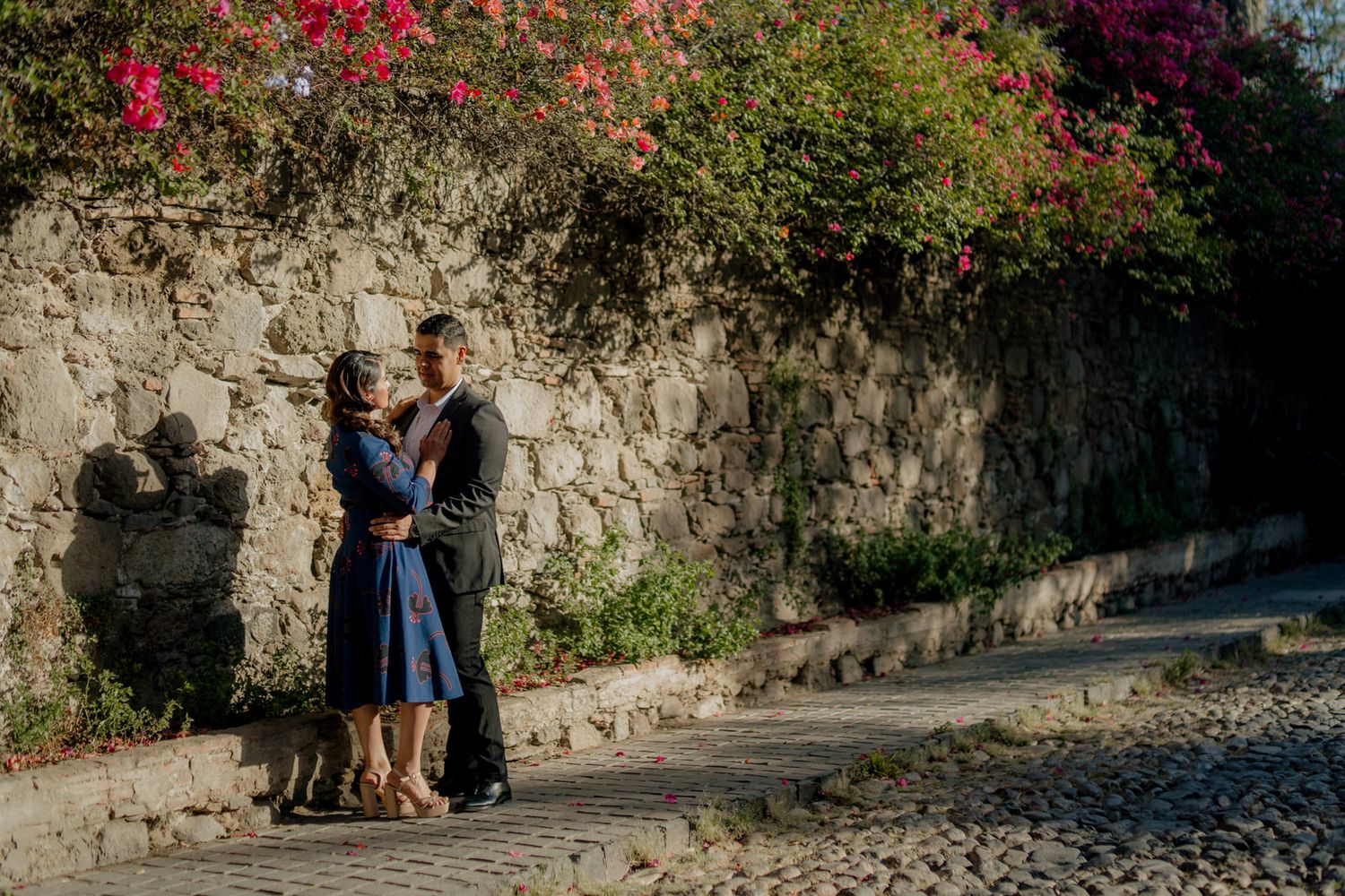 Couple sharing romantic moment by stone wall with flowering vines.