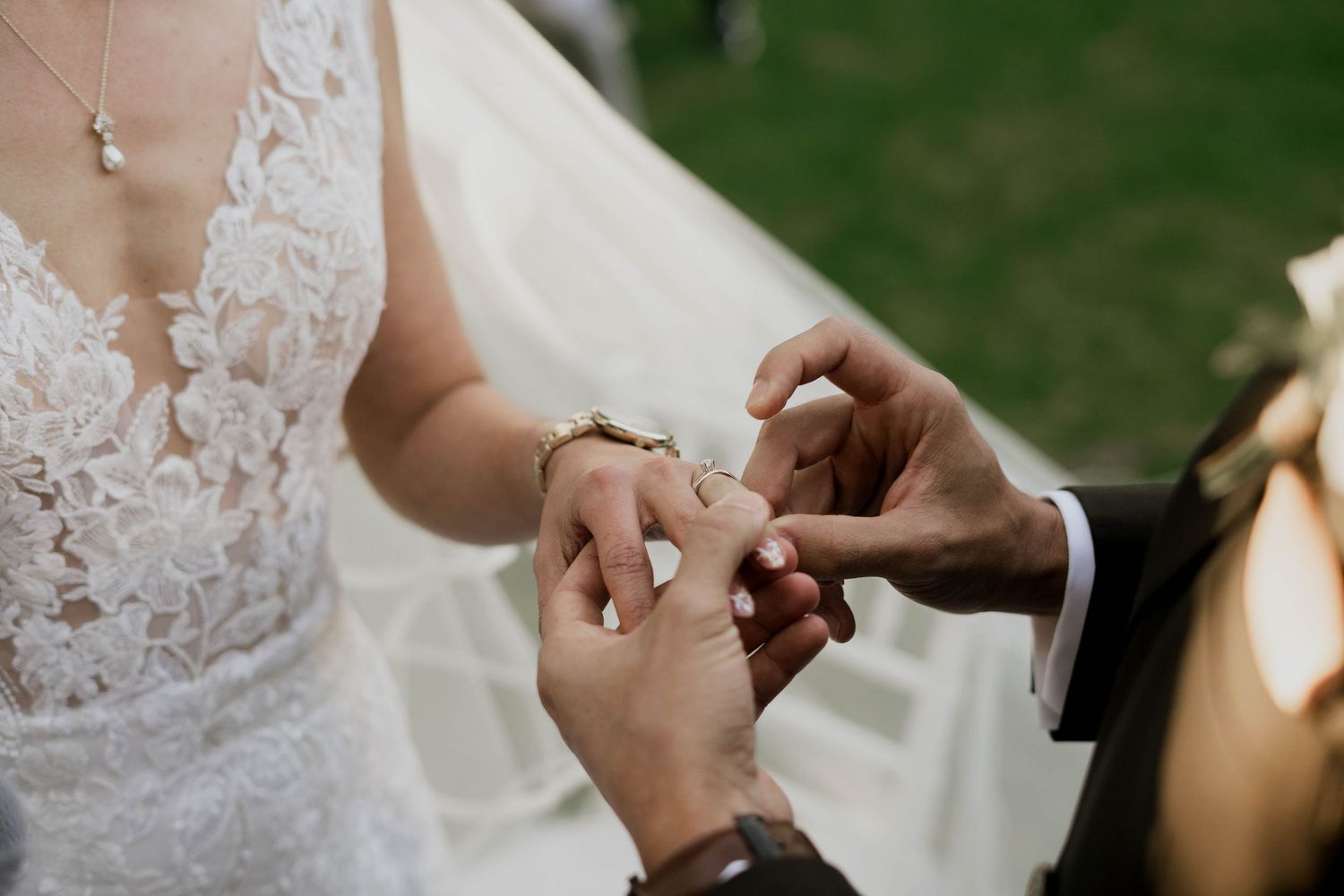 Close-up detail of delicate lace wedding dress against green outdoor background.