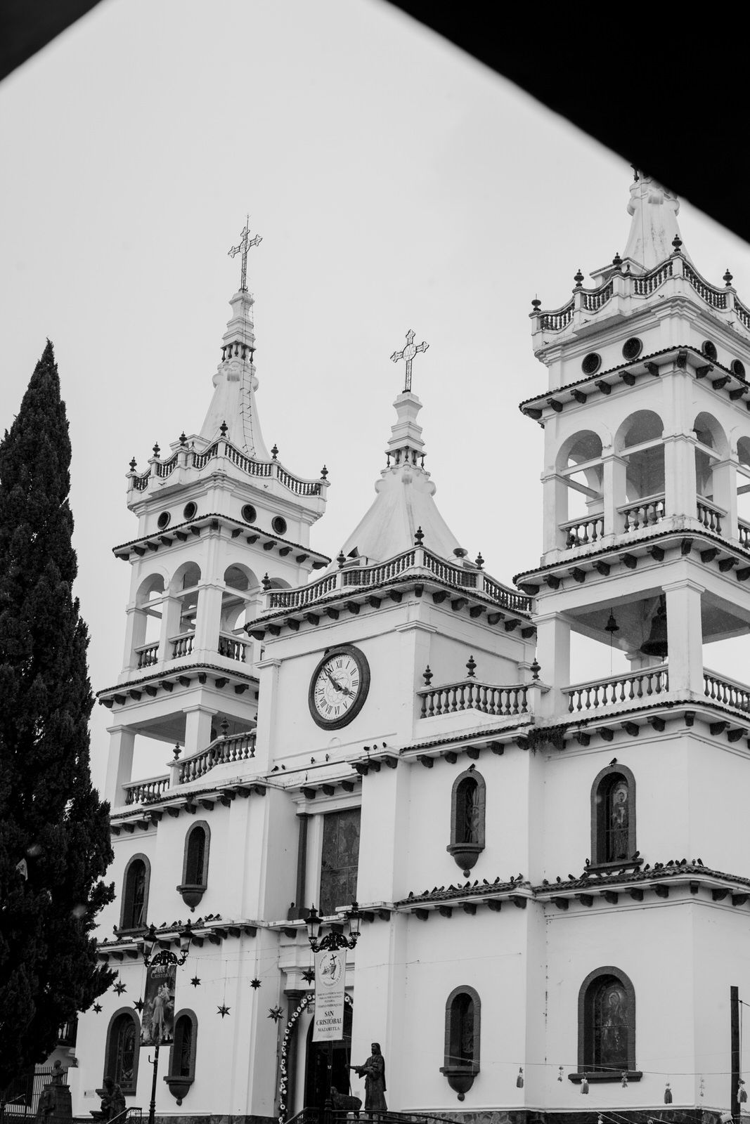 White colonial church facade with ornate bell towers and crosses against cloudy sky.