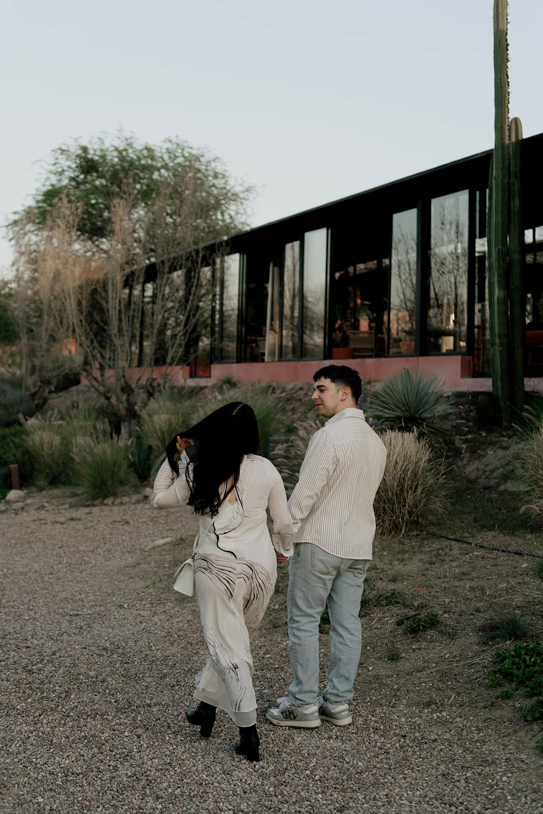 Two people walking together on a gravel path near modern buildings at dusk.