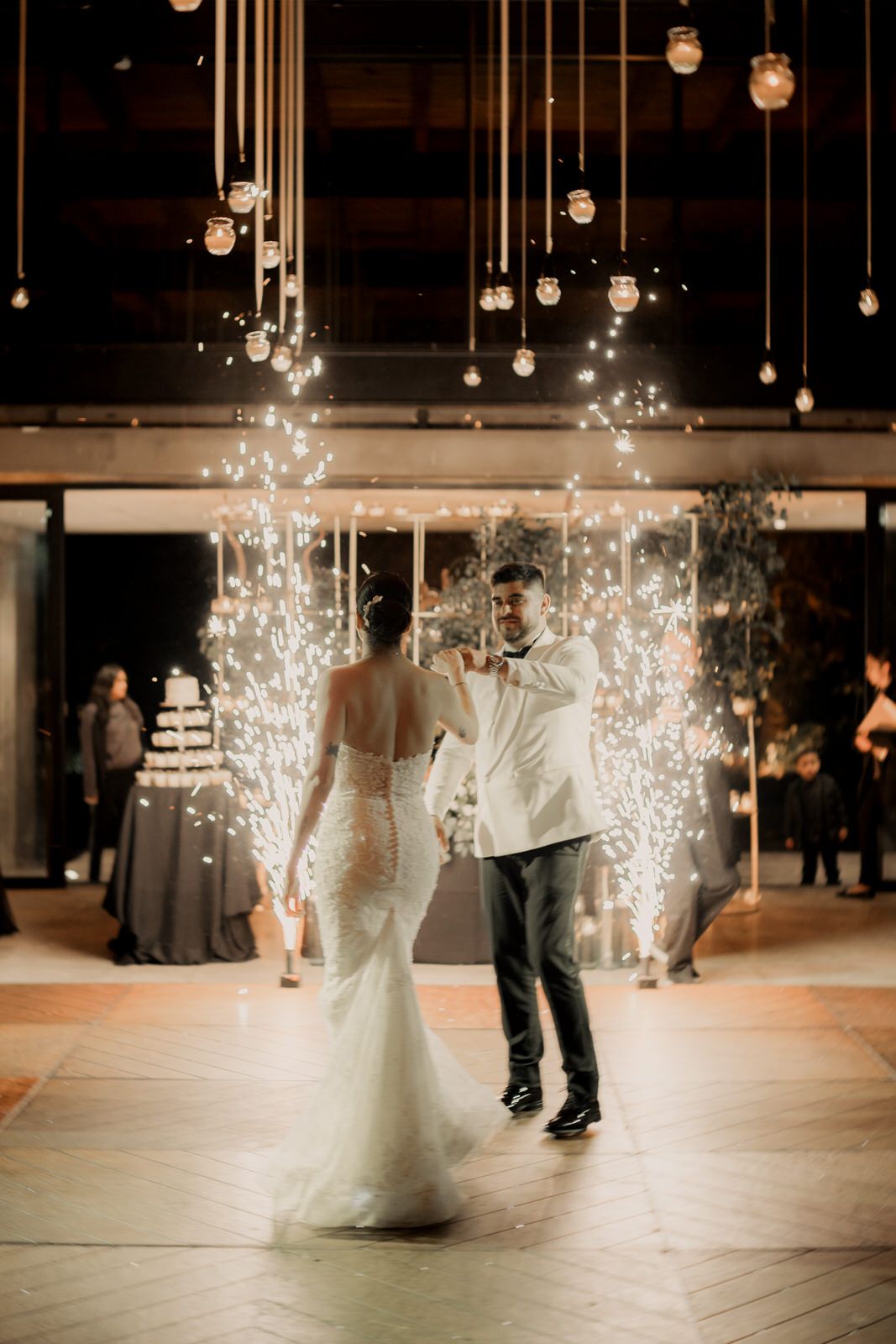 Wedding guests dance under suspended lights while sparklers create a magical effect on the dance floor.