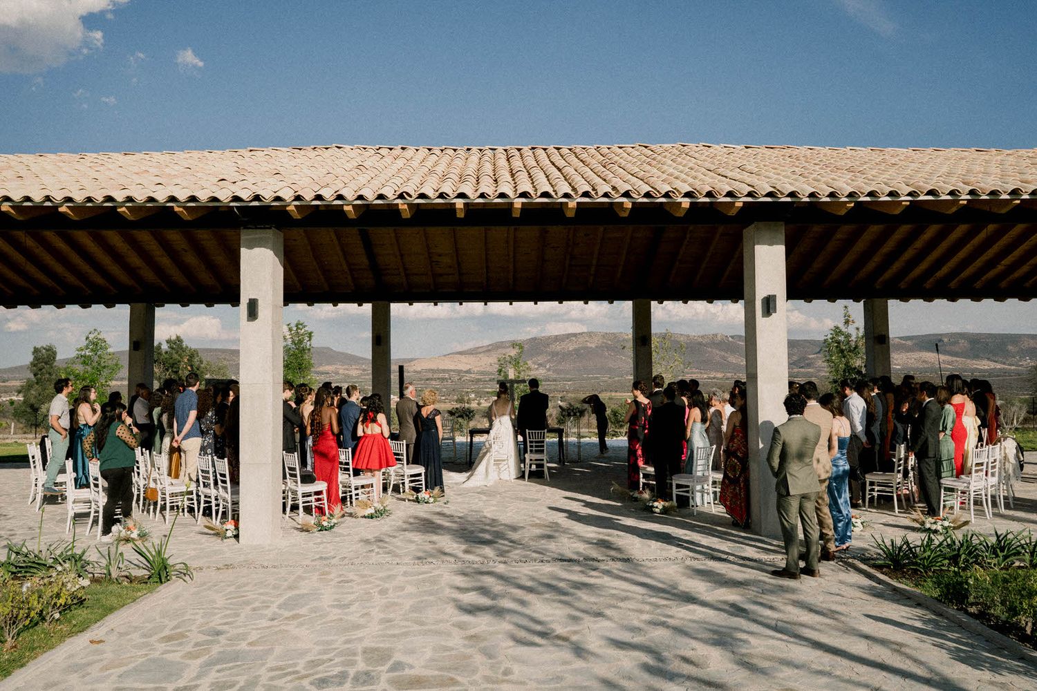 Panoramic view of an outdoor wedding ceremony space with white chairs and mountain backdrop.