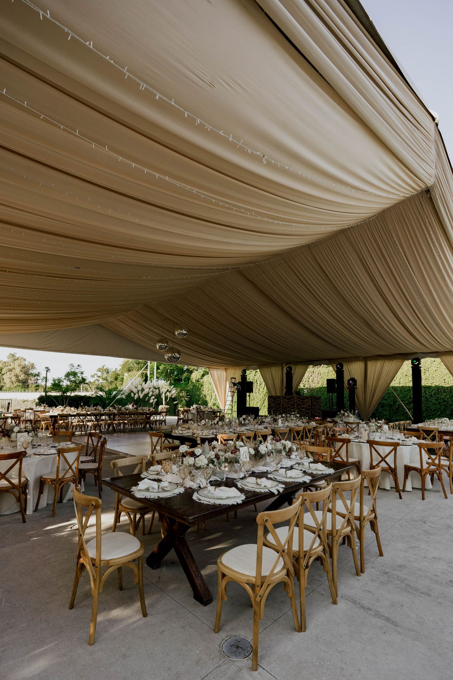 Spacious wedding venue with cream fabric ceiling draping and wooden cross-back chairs arranged at round tables.