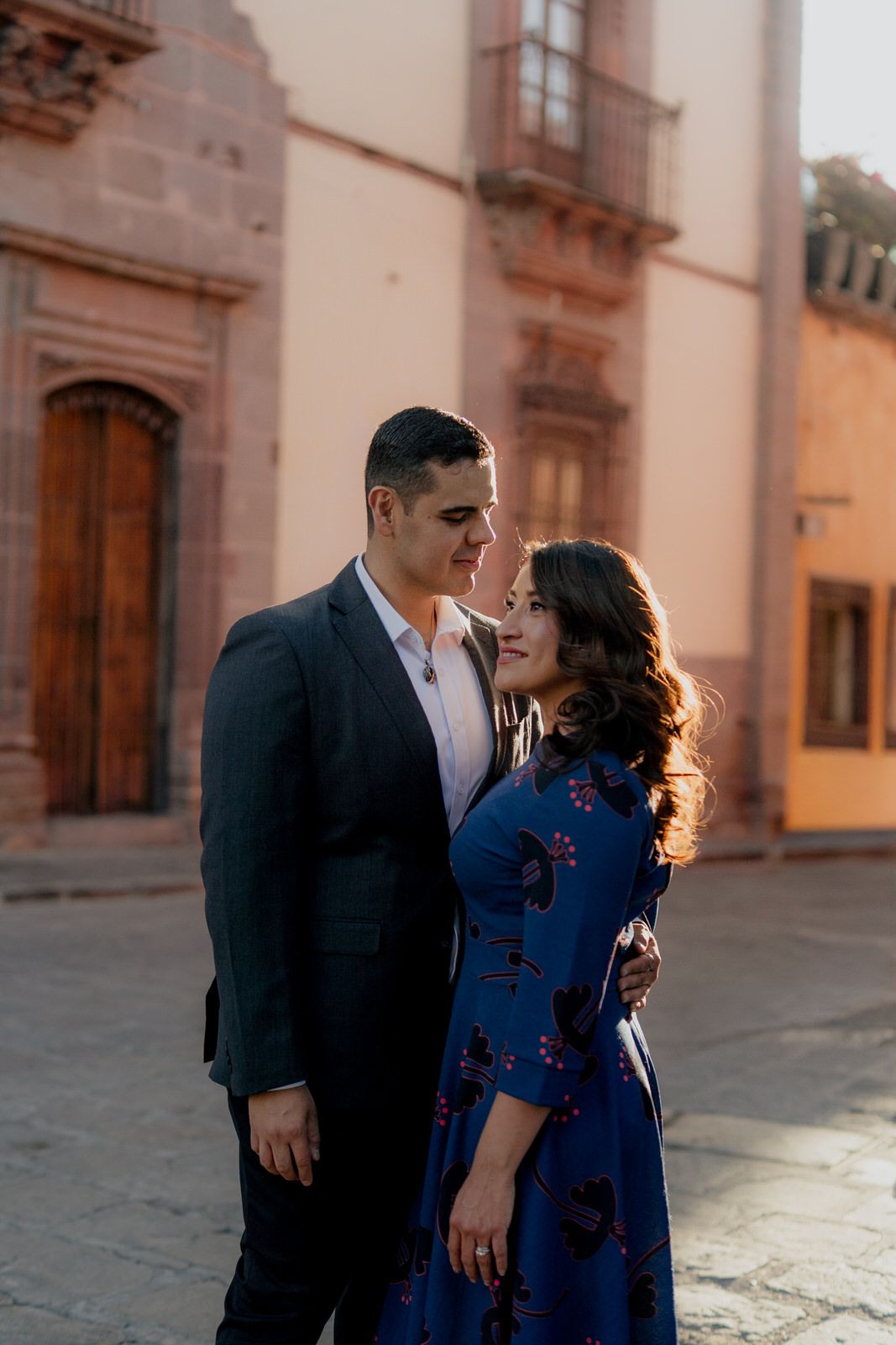 A romantic couple shares an intimate moment outside a historic building with ornate architecture.