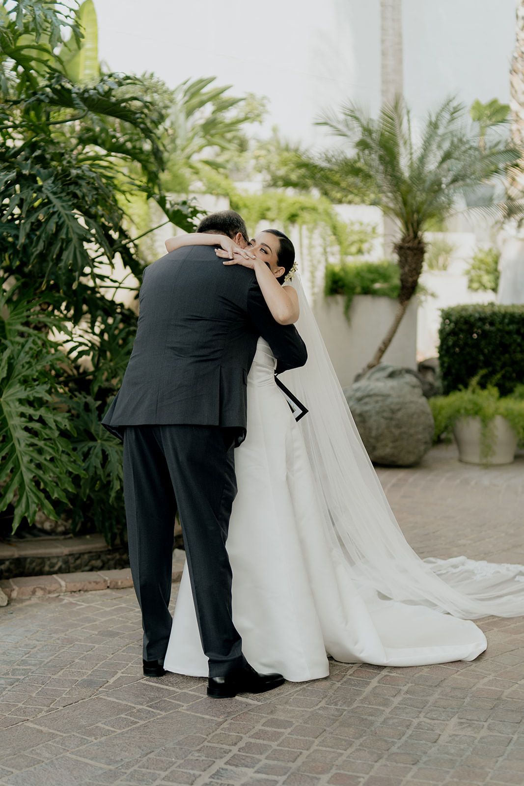 Bride and groom share an emotional first look embrace outdoors, surrounded by lush tropical greenery on their wedding day.