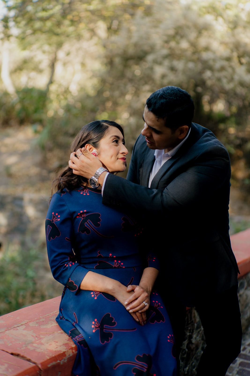 Tender moment between couple in formal attire sitting on red brick ledge.