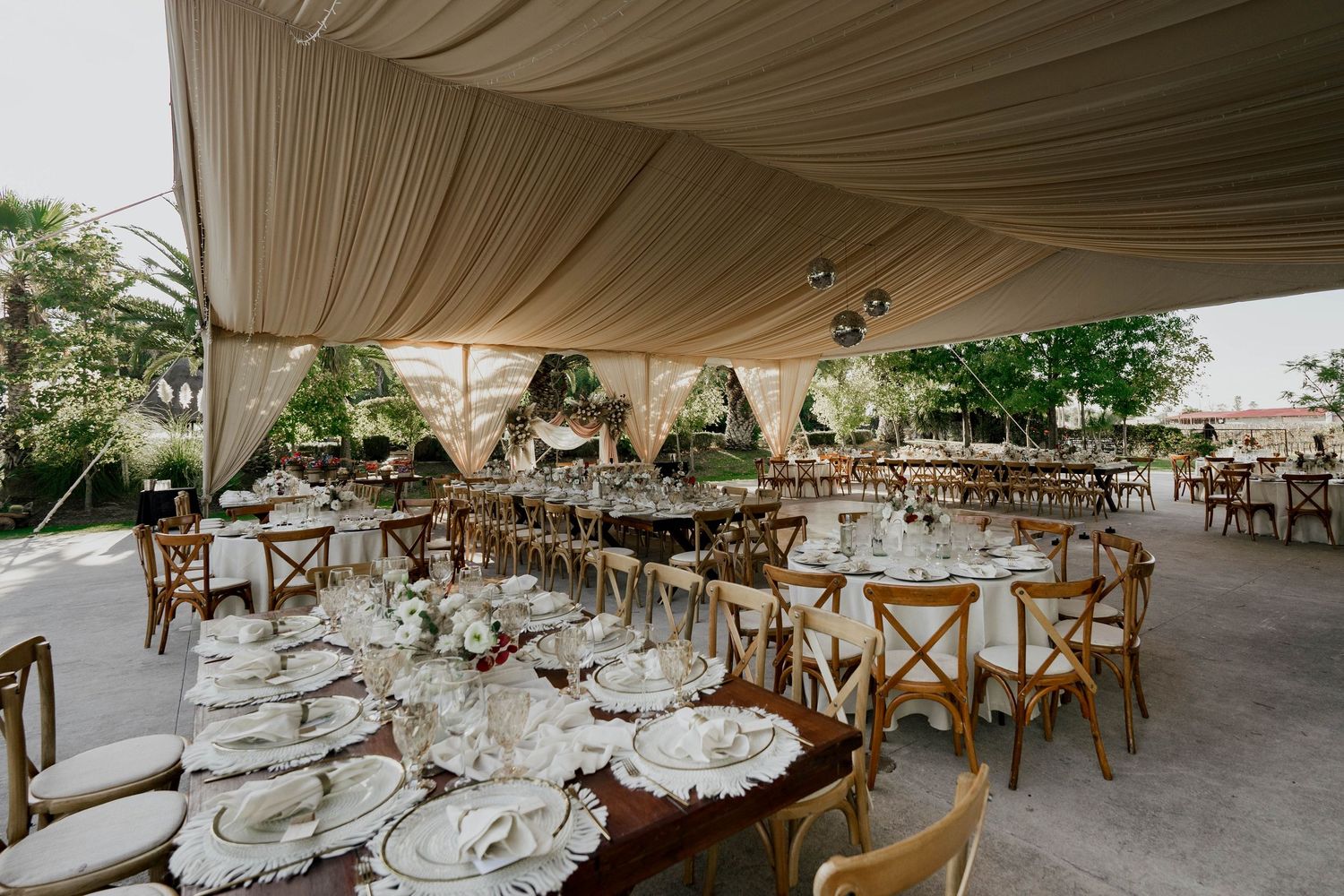 Large outdoor wedding reception tent with rustic wooden chairs and white draped ceiling.