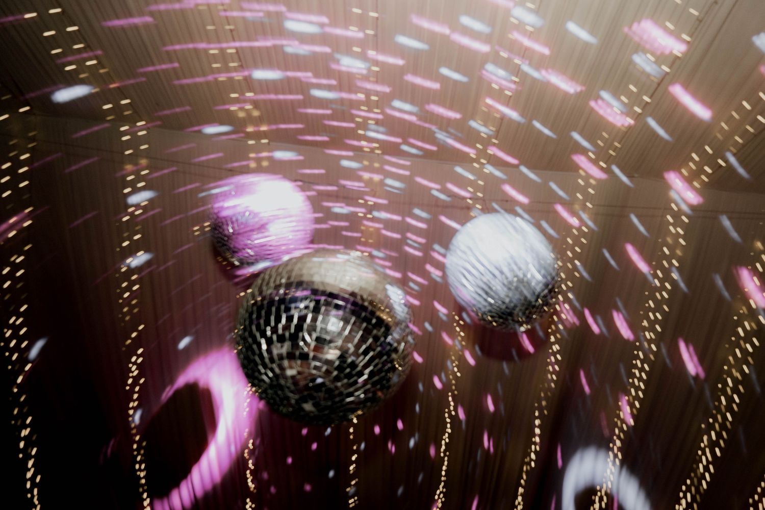 Disco balls spinning with purple and pink light reflections on a dance floor ceiling.