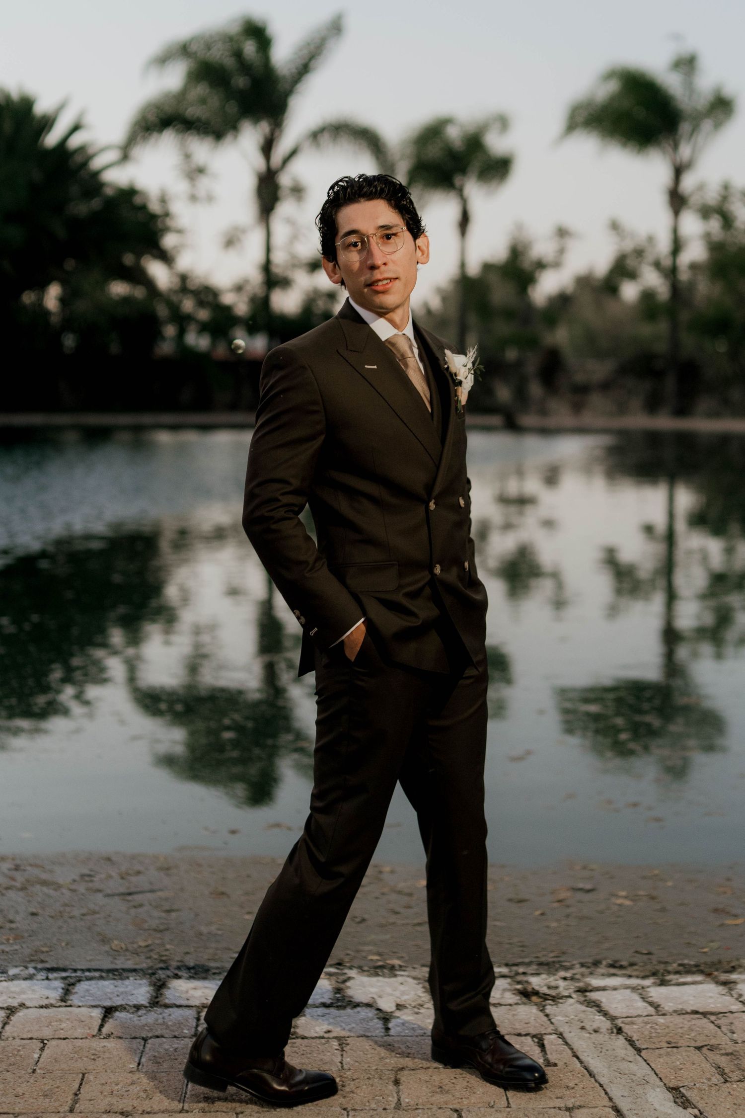 Ring bearer in formal attire poses playfully by a waterfront setting.