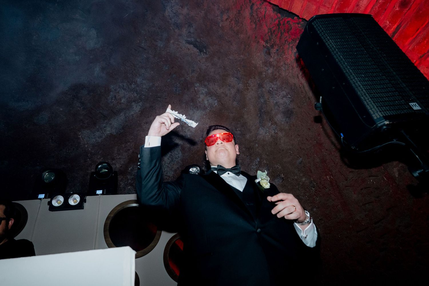 A party guest dances energetically under red lighting at a nighttime celebration.