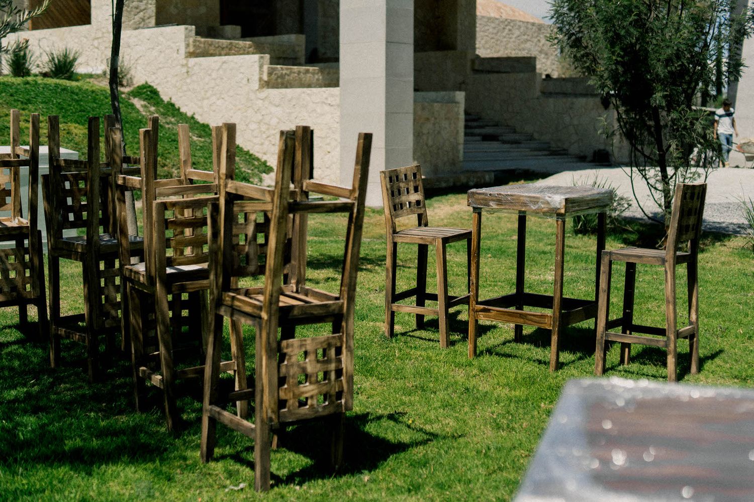 Wooden chairs stacked on a grassy lawn in front of a stone building.