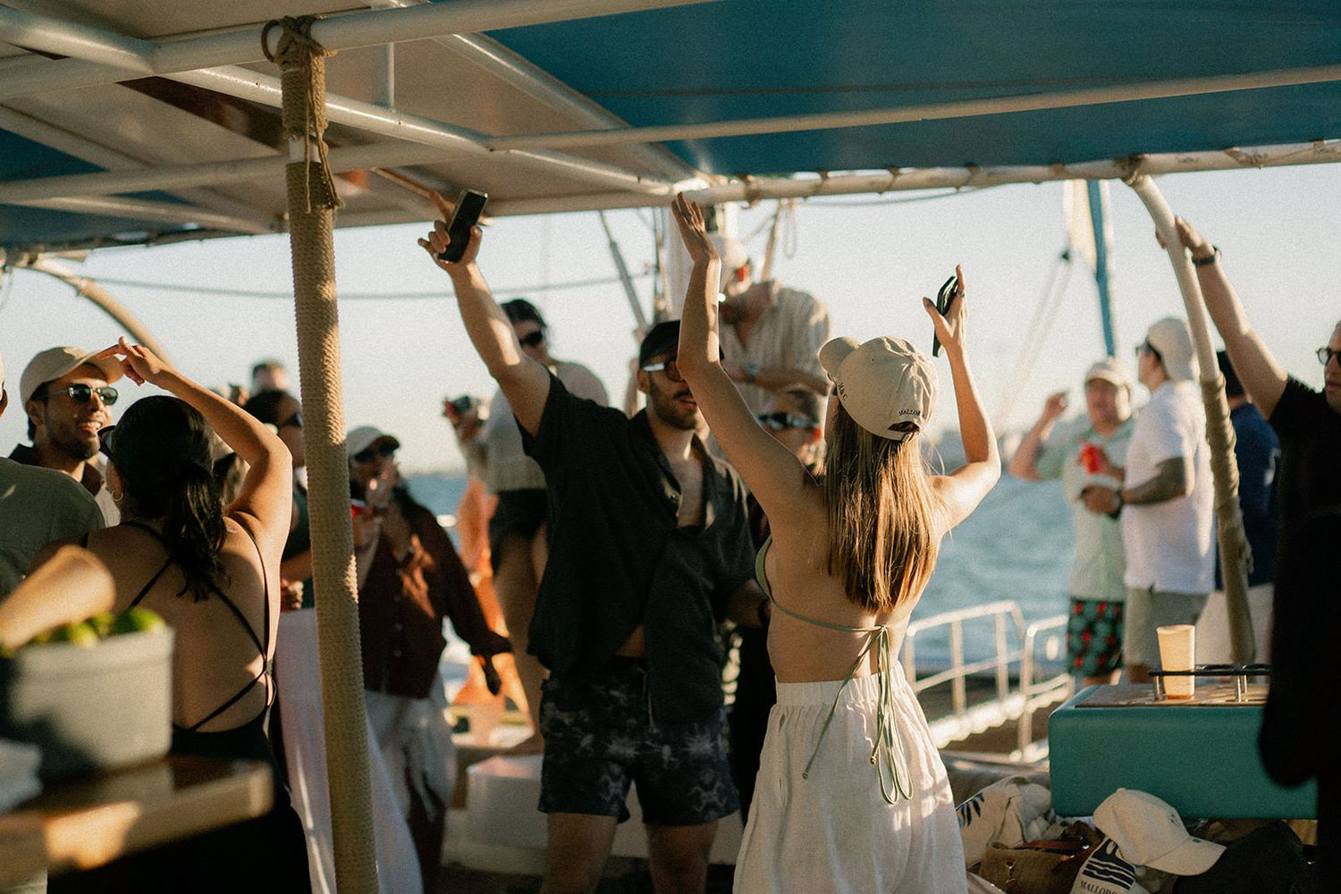 Party guests dance with raised arms on a boat deck during a sunset cruise celebration.