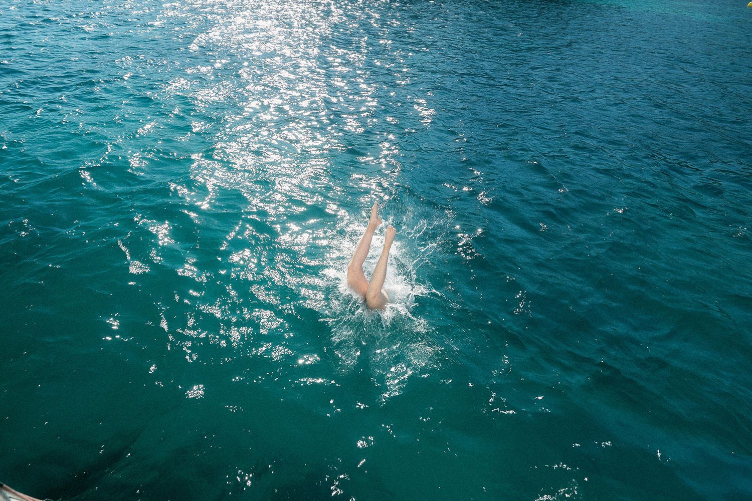 Person diving into crystal clear turquoise waters creating a splash against the sparkling ocean surface.